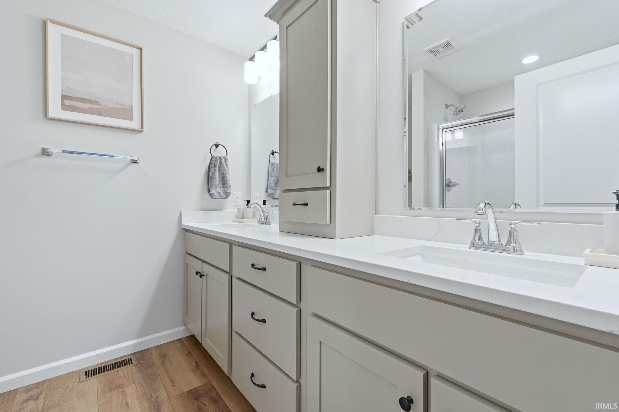 Full bathroom with double vanity, a stall shower, and light wood finished floors