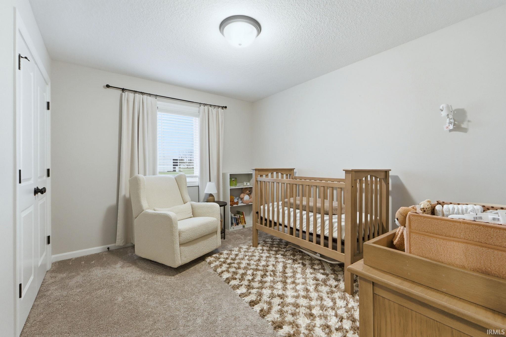Bedroom with a nursery area, light carpet, and a textured ceiling