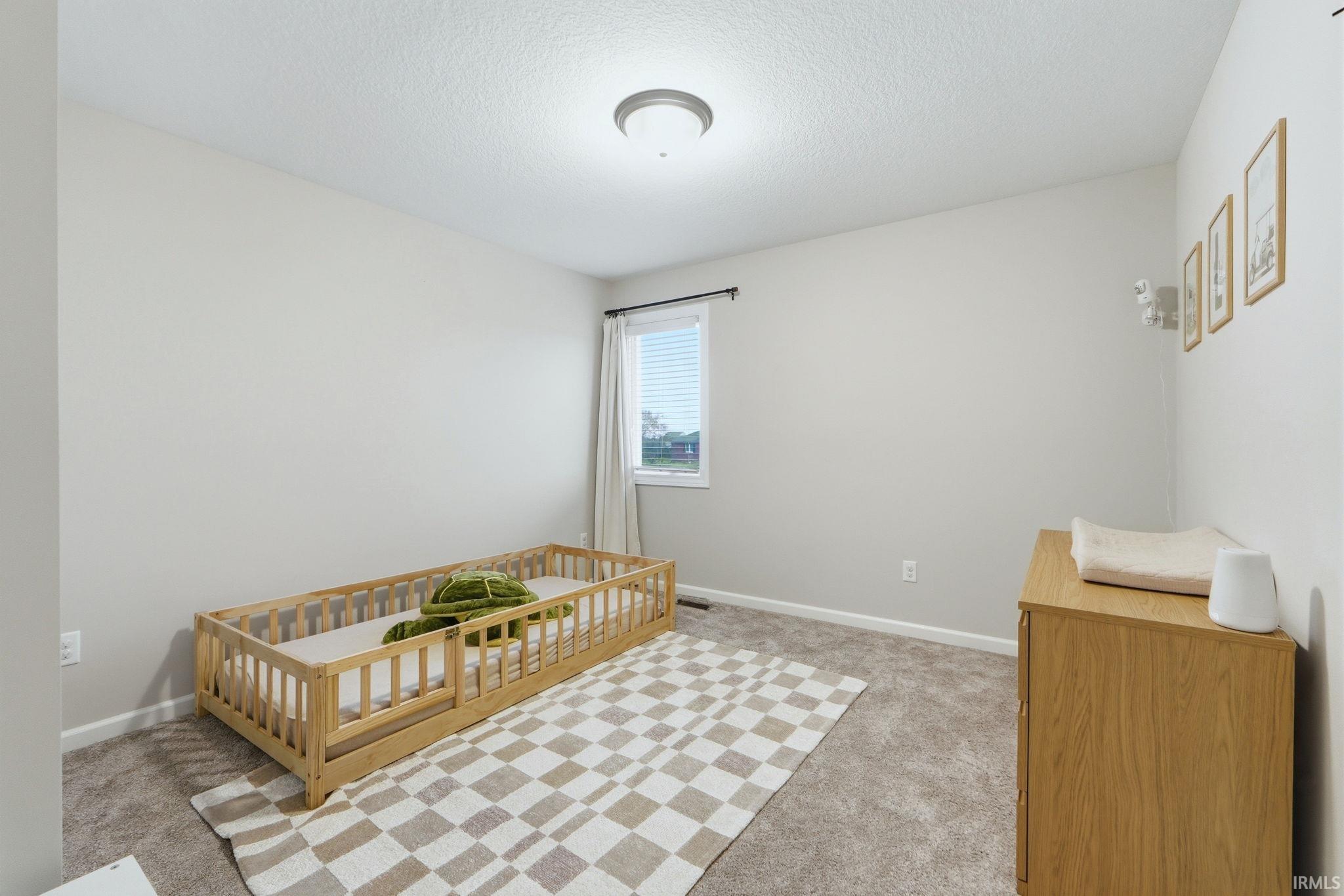 Bedroom with light colored carpet, a crib, and a textured ceiling