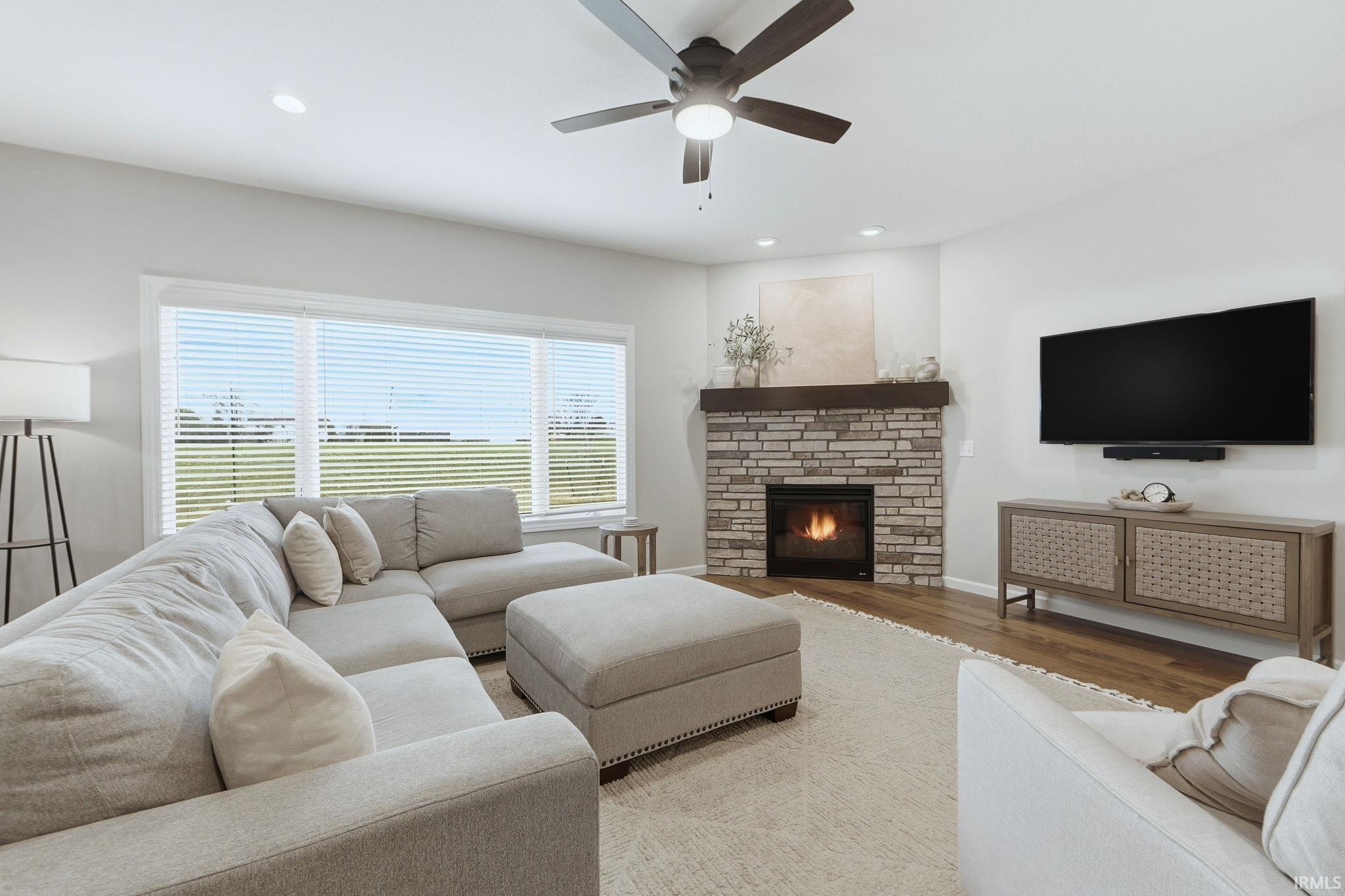 Living area with wood finished floors, a ceiling fan, a brick fireplace, and recessed lighting