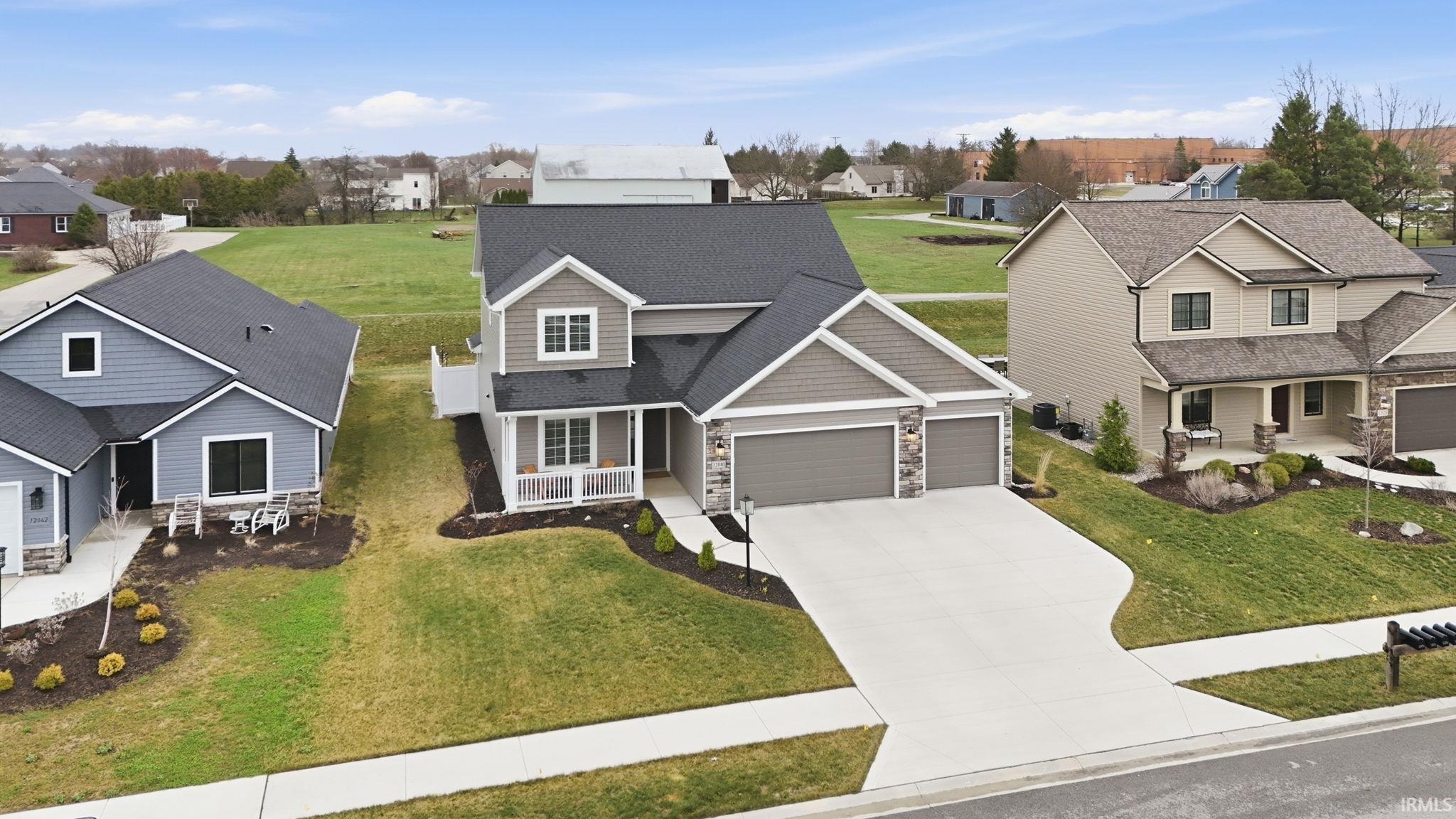Traditional home with stone siding, an attached garage, a porch, a front lawn, and driveway