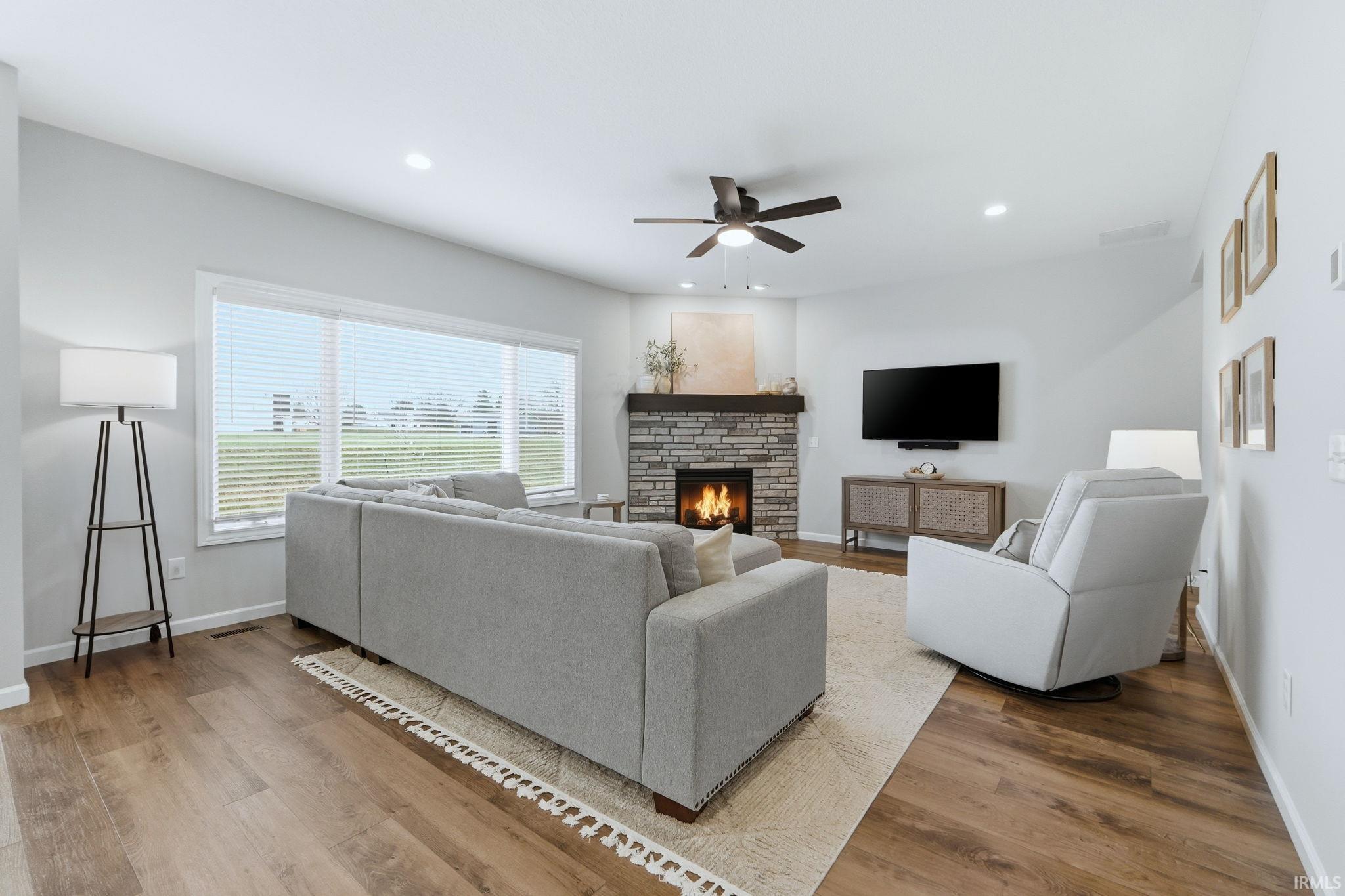 Living area with light wood-type flooring, a ceiling fan, a stone fireplace, and recessed lighting
