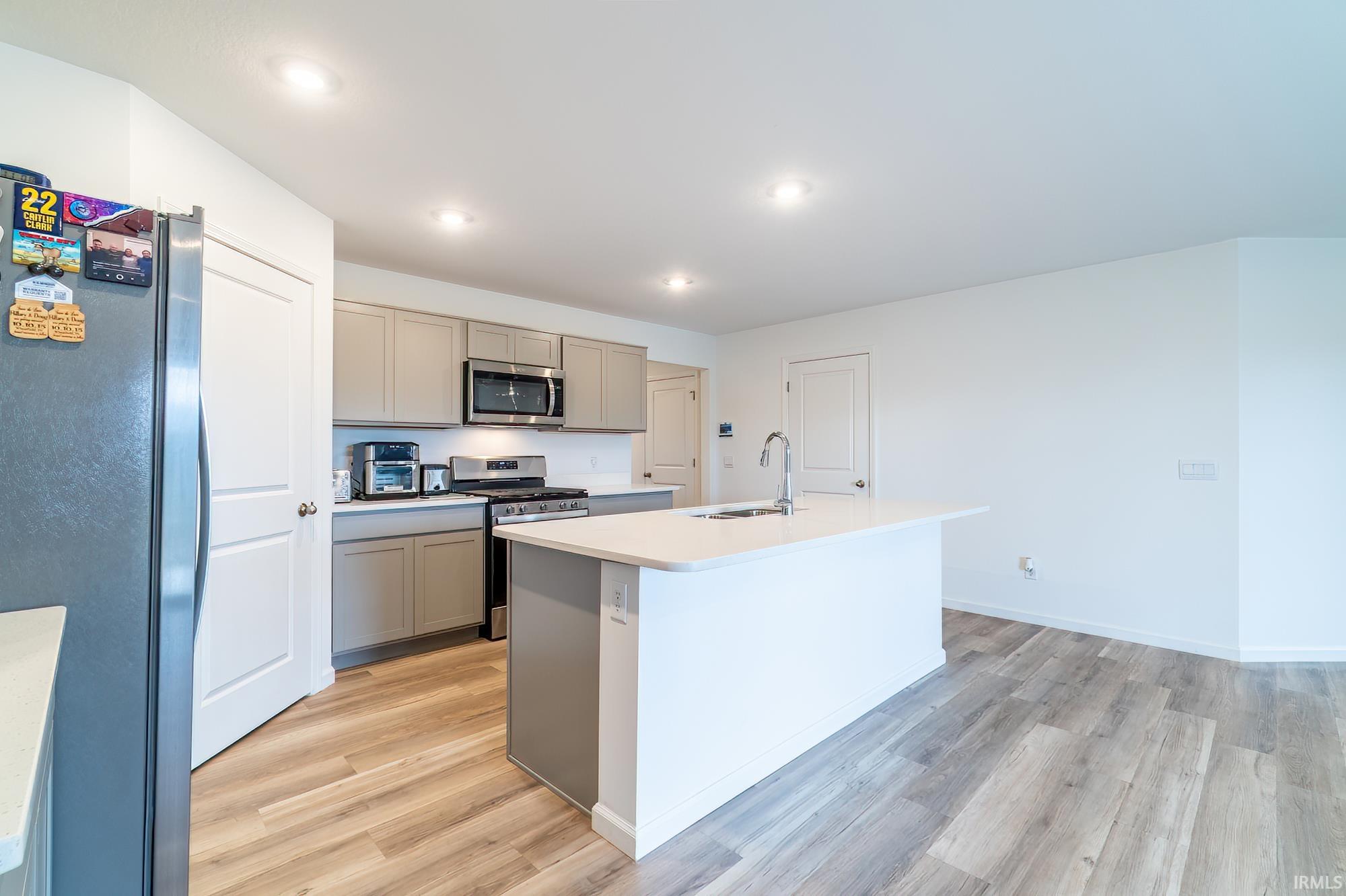 Kitchen with stainless steel appliances, light countertops, an island with sink, light wood finished floors, and recessed lighting