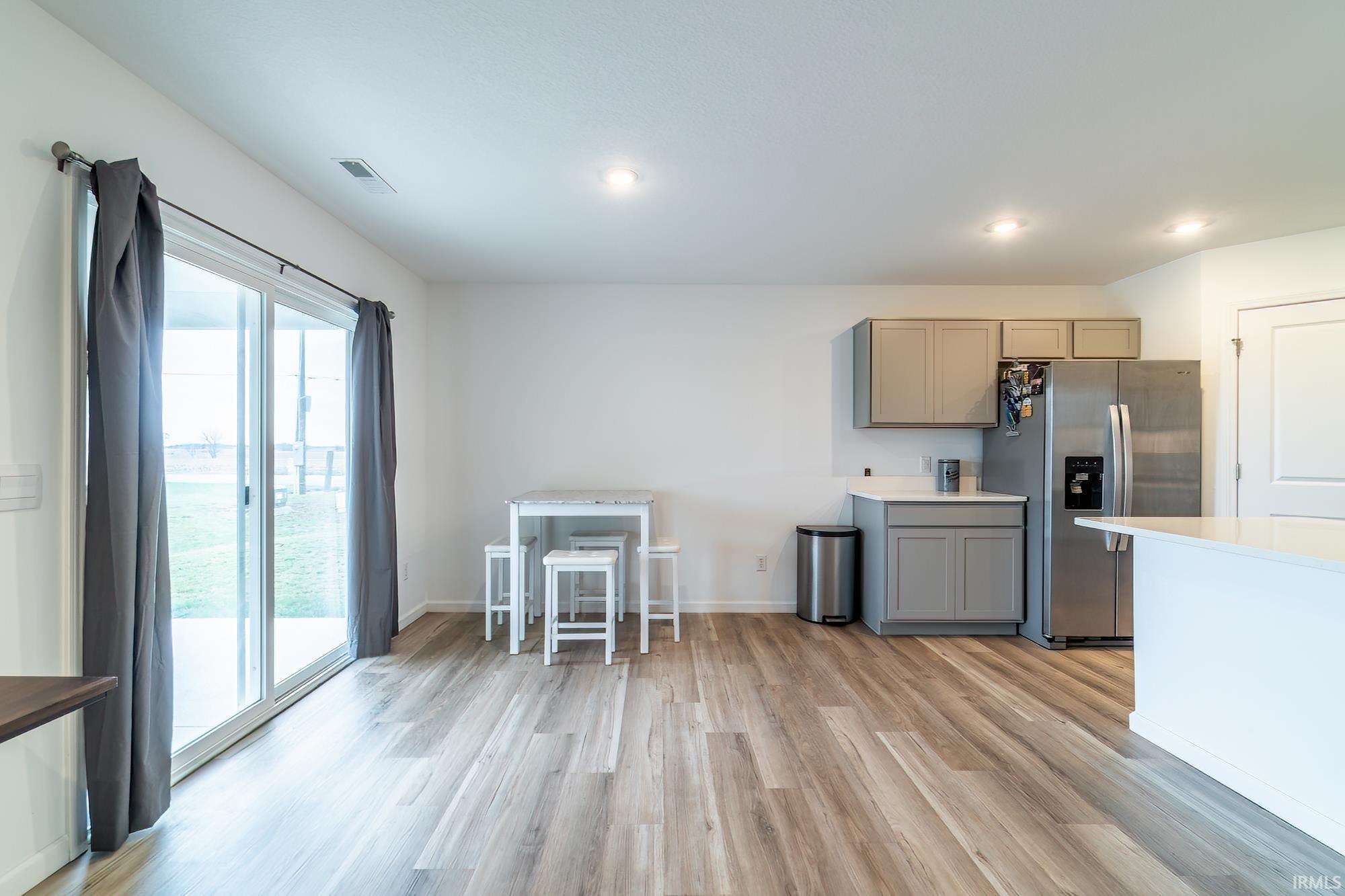 Kitchen with gray cabinets, stainless steel refrigerator with ice dispenser, light wood-style floors, and recessed lighting