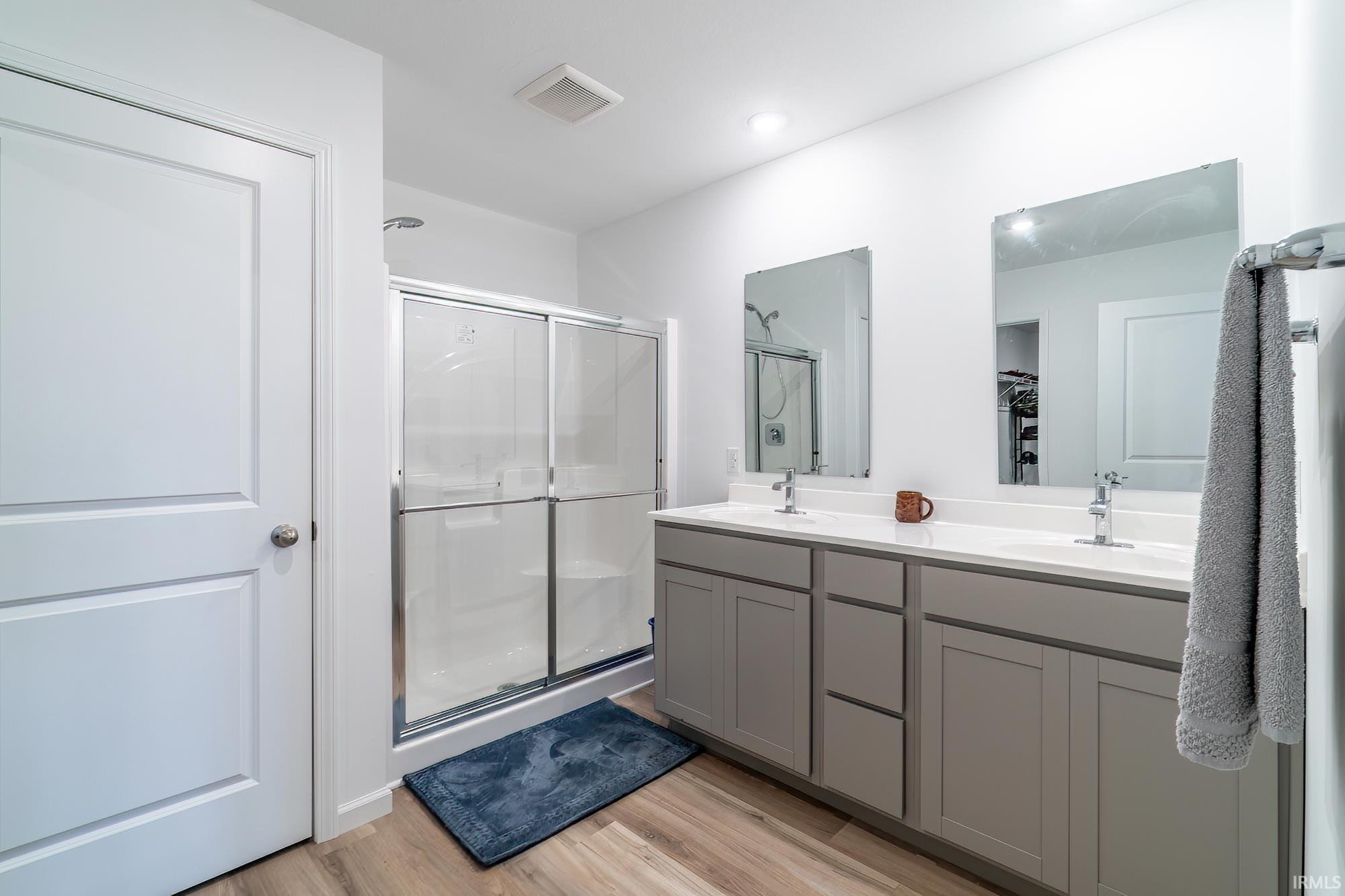 Full bath with double vanity, a shower stall, and light wood-type flooring