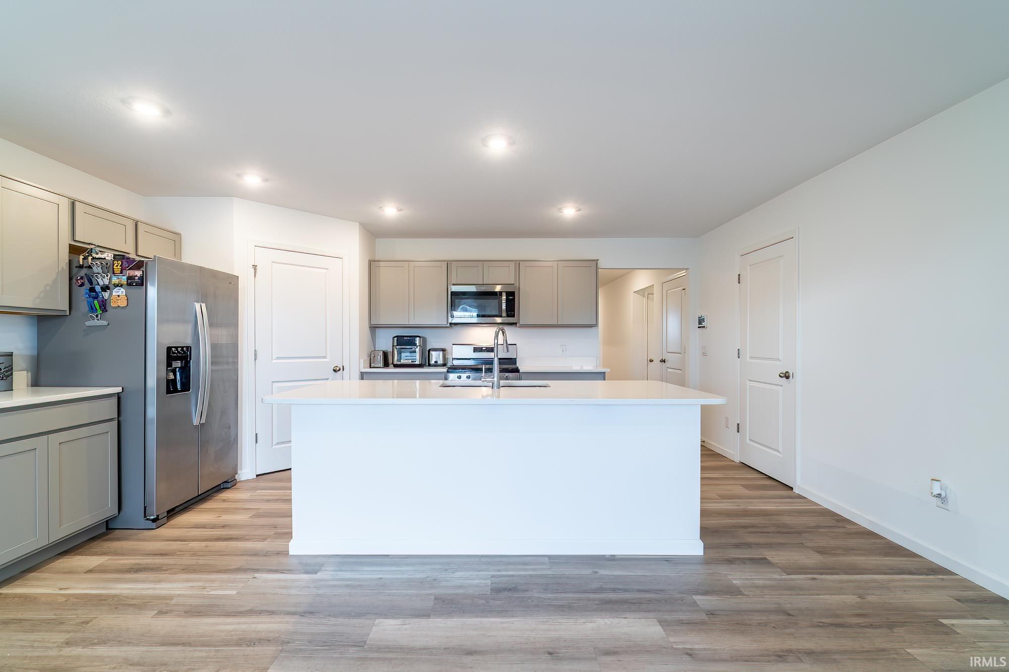 Kitchen with gray cabinets, stainless steel appliances, light wood-type flooring, an island with sink, and recessed lighting