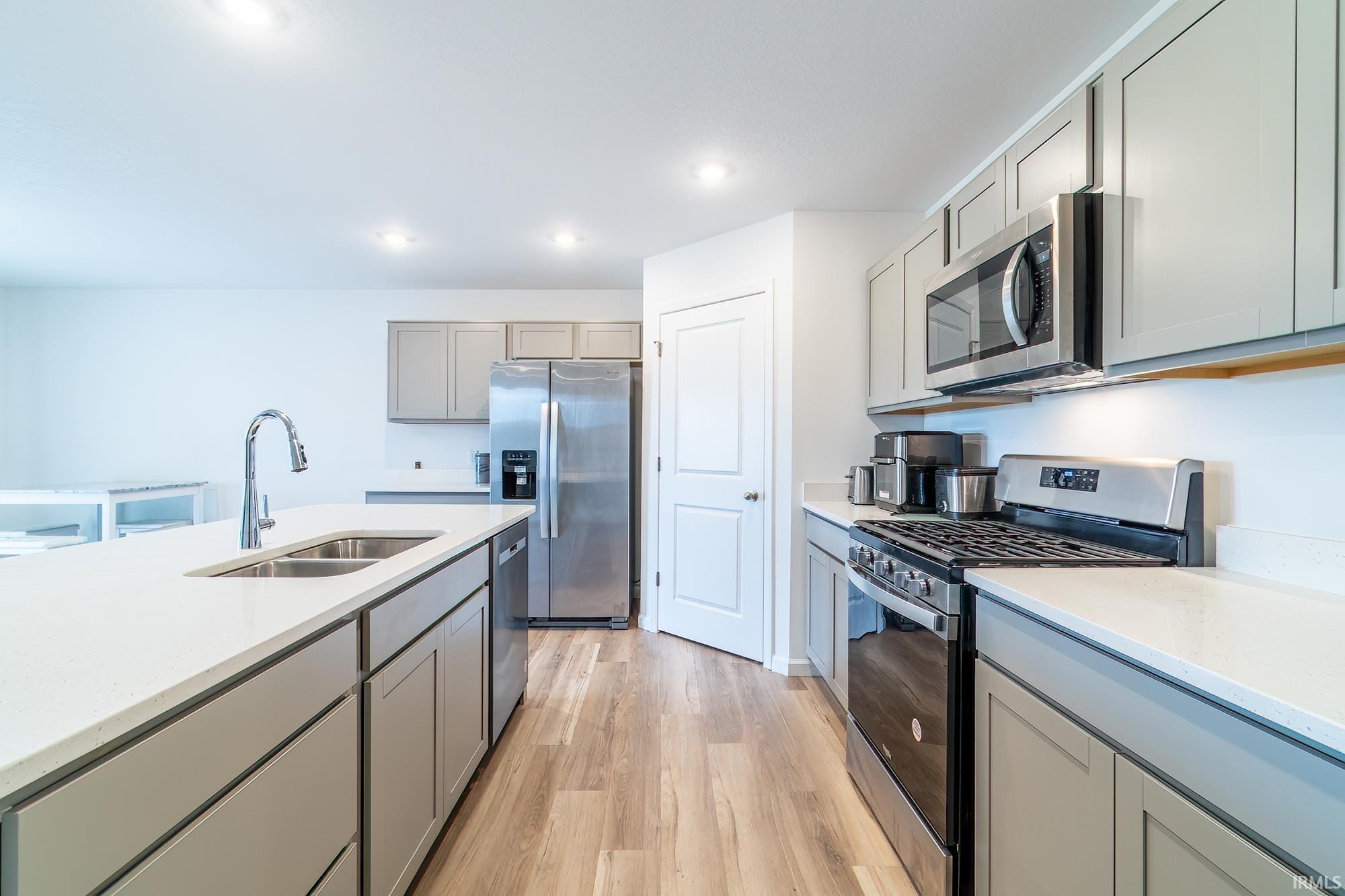Kitchen featuring gray cabinets, stainless steel appliances, light wood finished floors, light stone counters, and recessed lighting