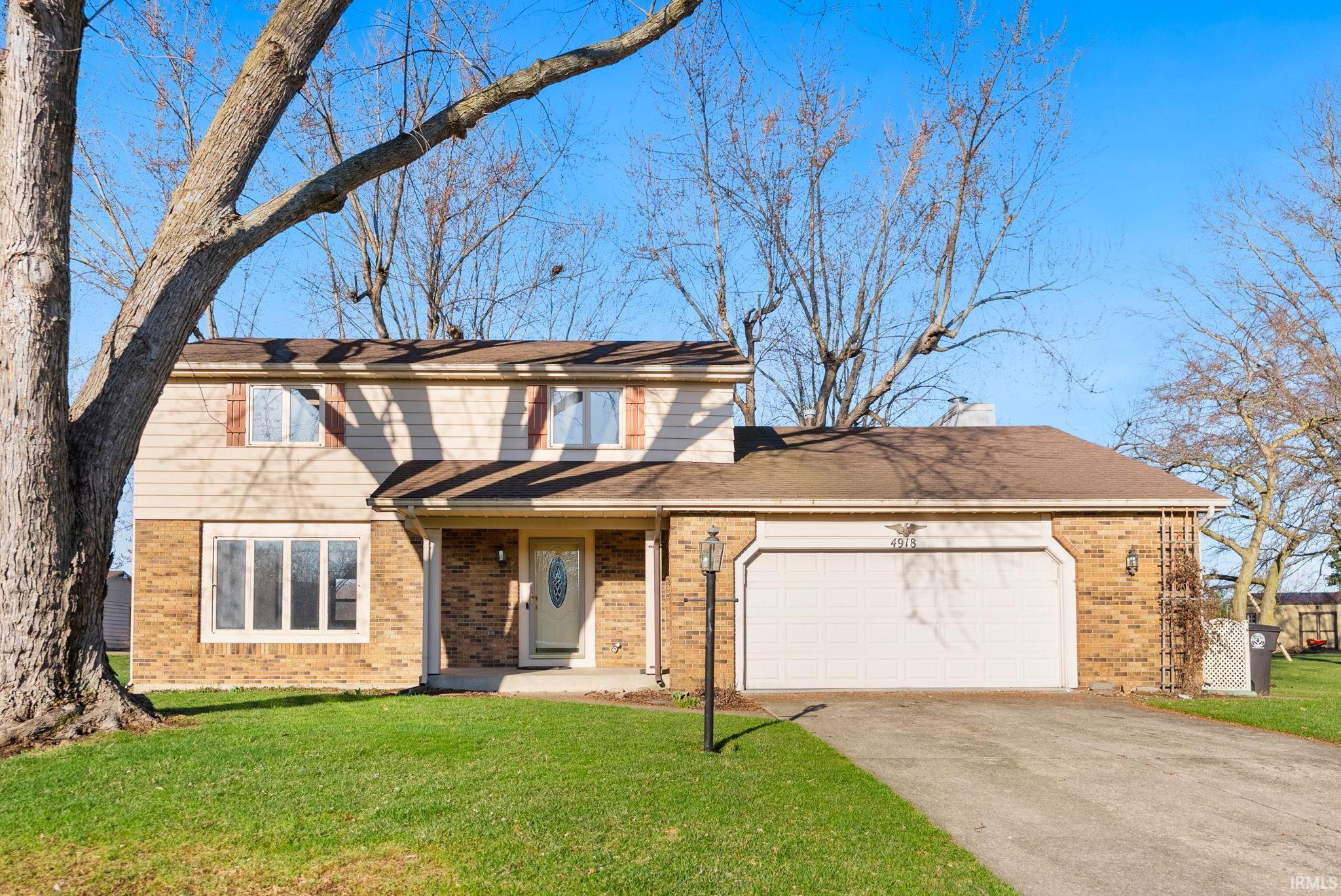 Traditional-style house featuring brick siding, a garage, driveway, and a front lawn