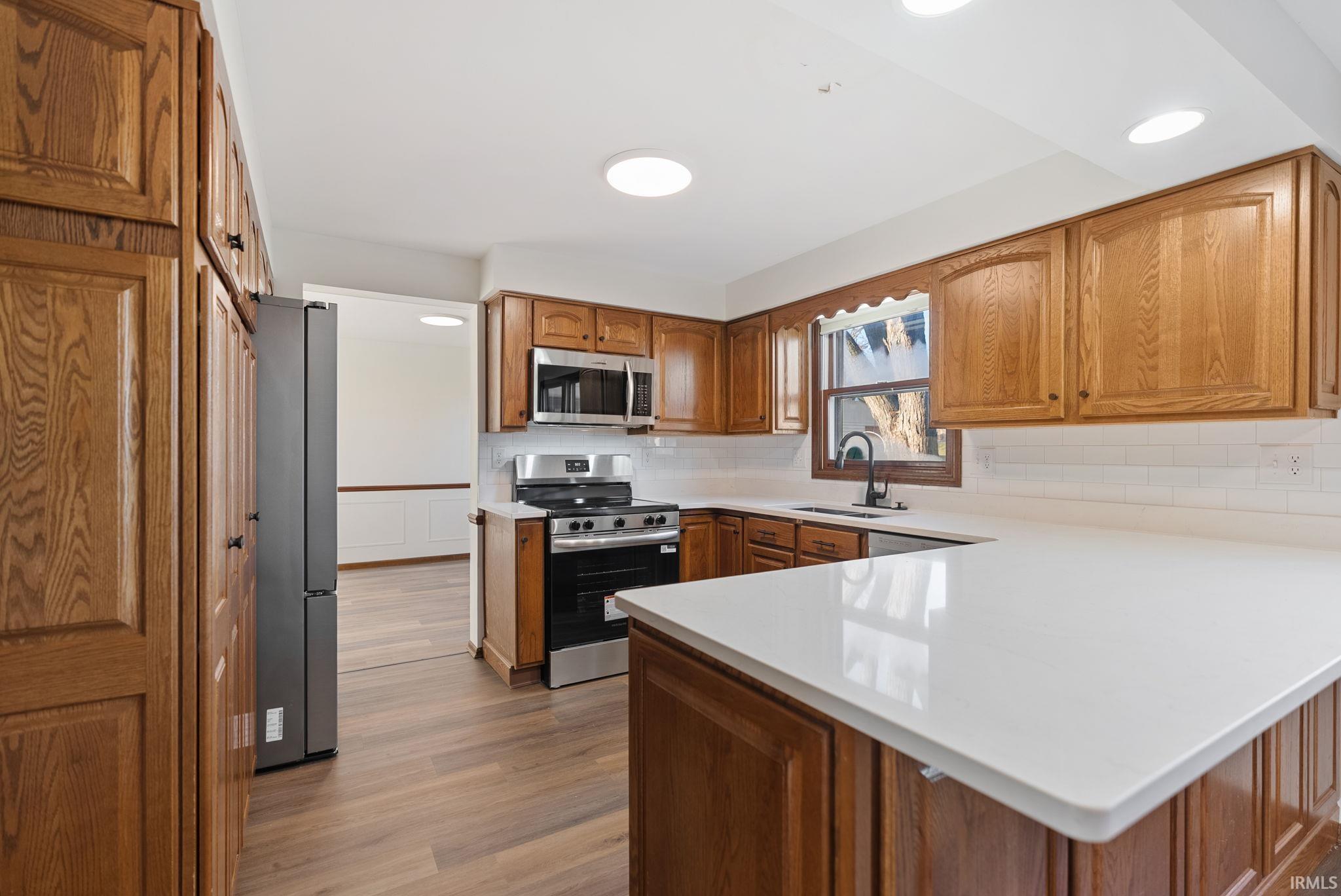 Kitchen with wood finish cabinets, stainless steel appliances, a peninsula, dark wood finished floors, and backsplash