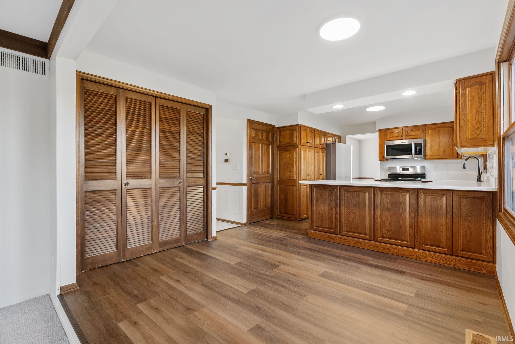 Kitchen with light countertops, wood finish cabinetry, light wood-style flooring, a peninsula, and stainless steel appliances