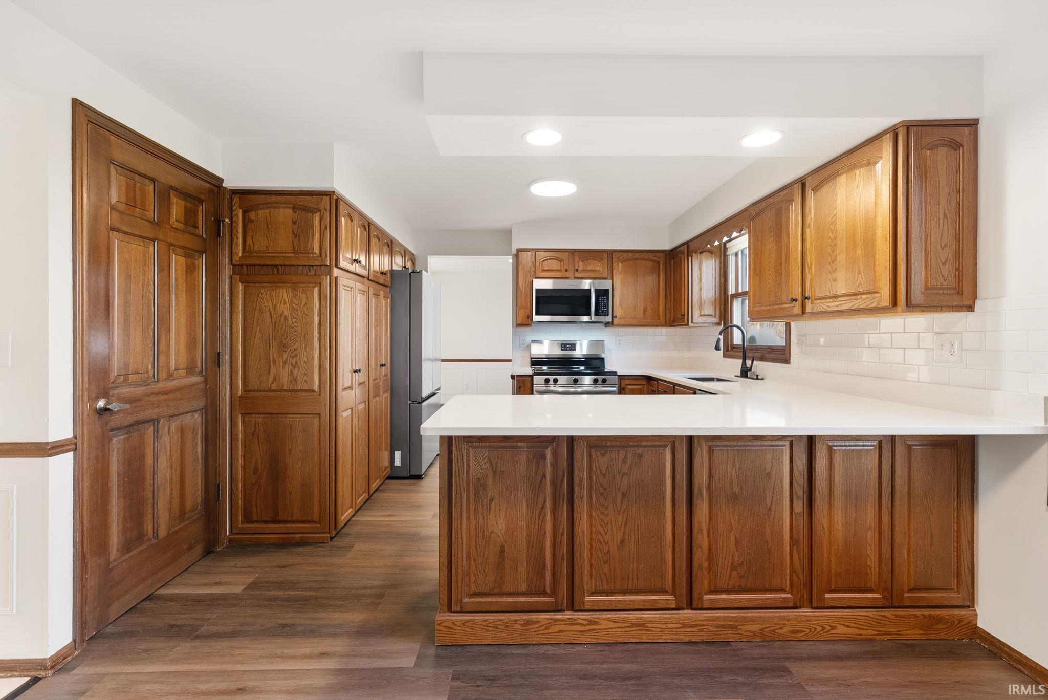 Kitchen with wood finish cabinets, a peninsula, stainless steel appliances, dark wood finished floors, and recessed lighting