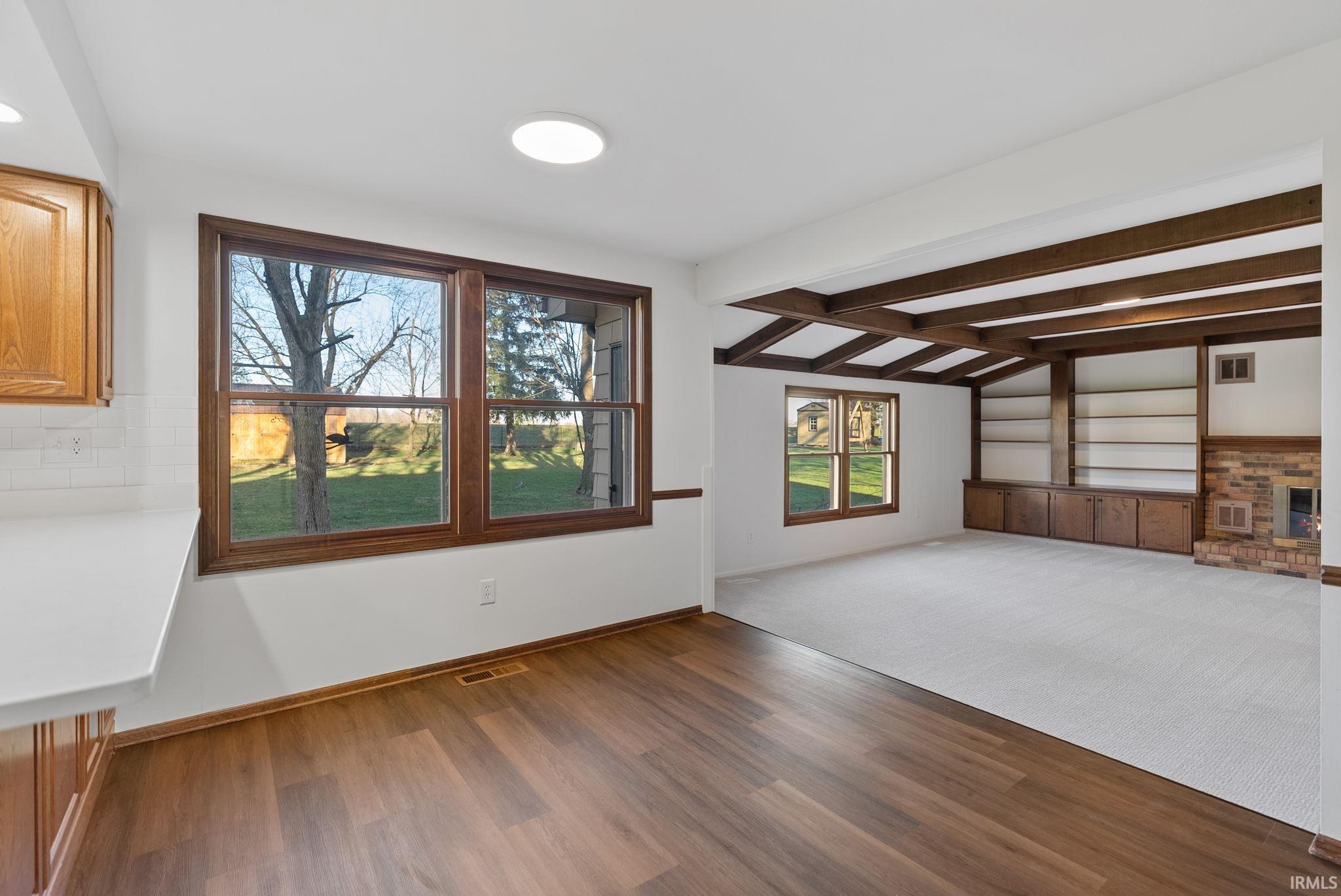 Unfurnished living room featuring plenty of natural light, lofted ceiling with beams, dark wood-style flooring, a fireplace, and dark carpet