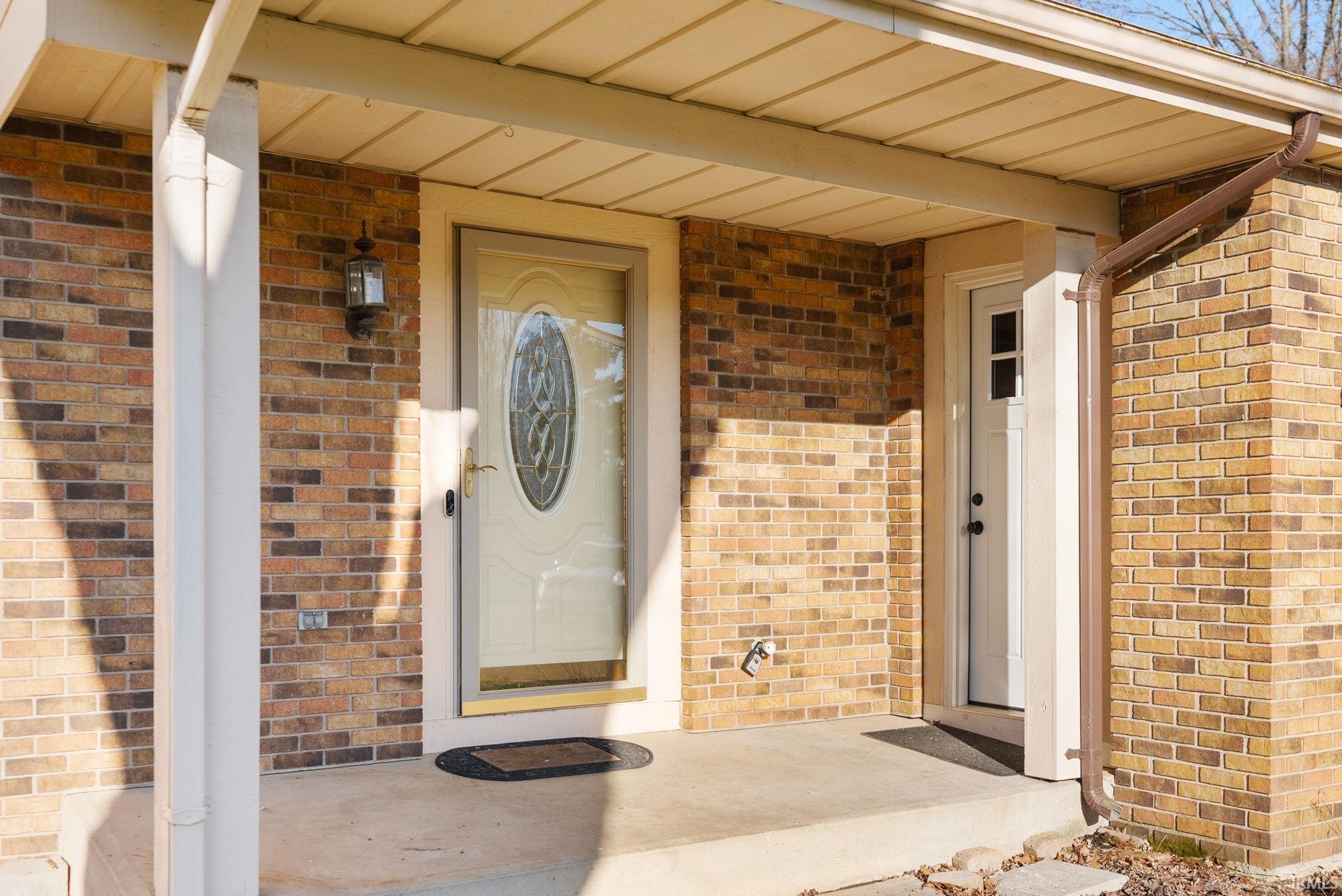 Doorway to property featuring brick siding and covered porch