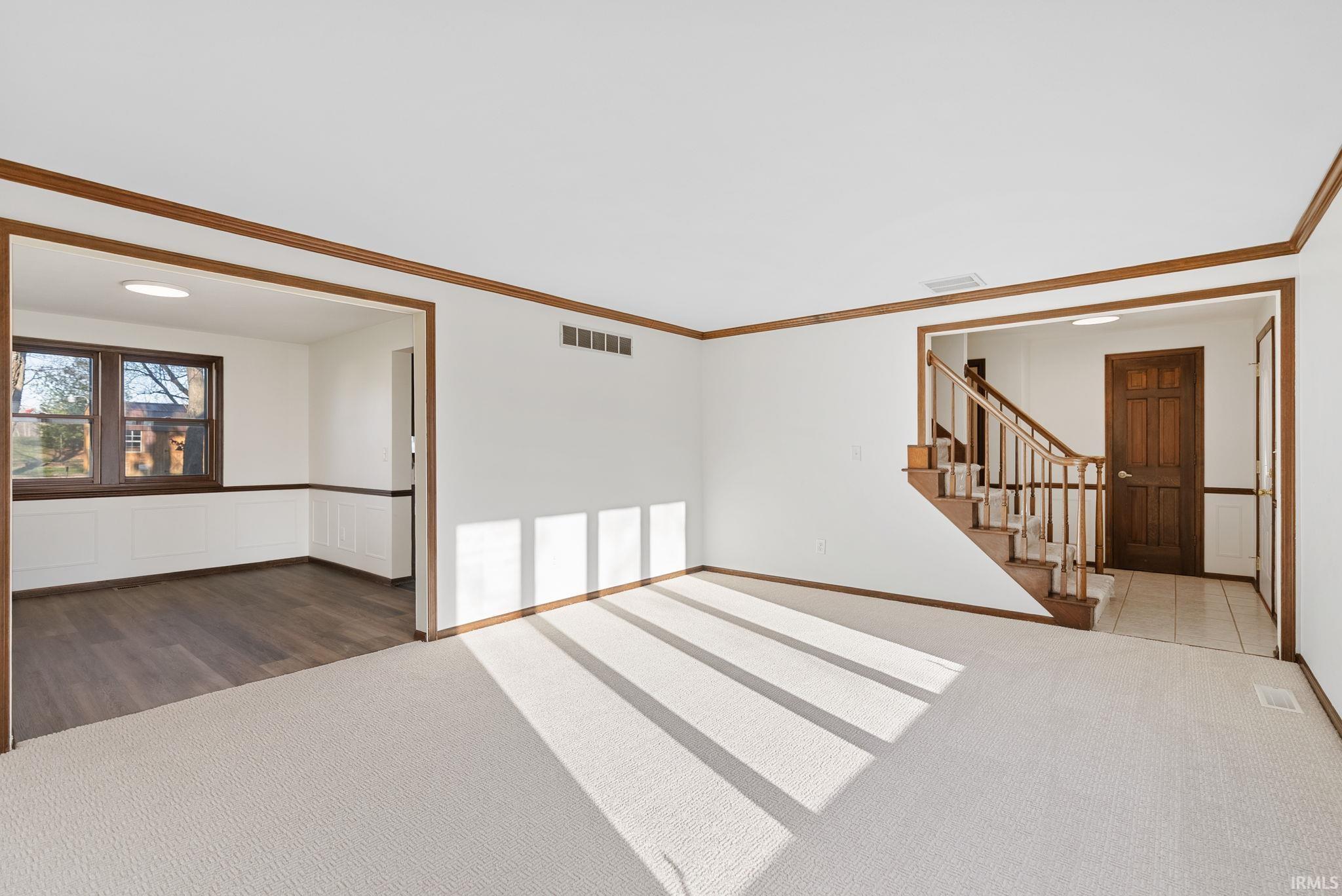 Unfurnished room with dark colored carpet, crown molding, and a wainscoted wall