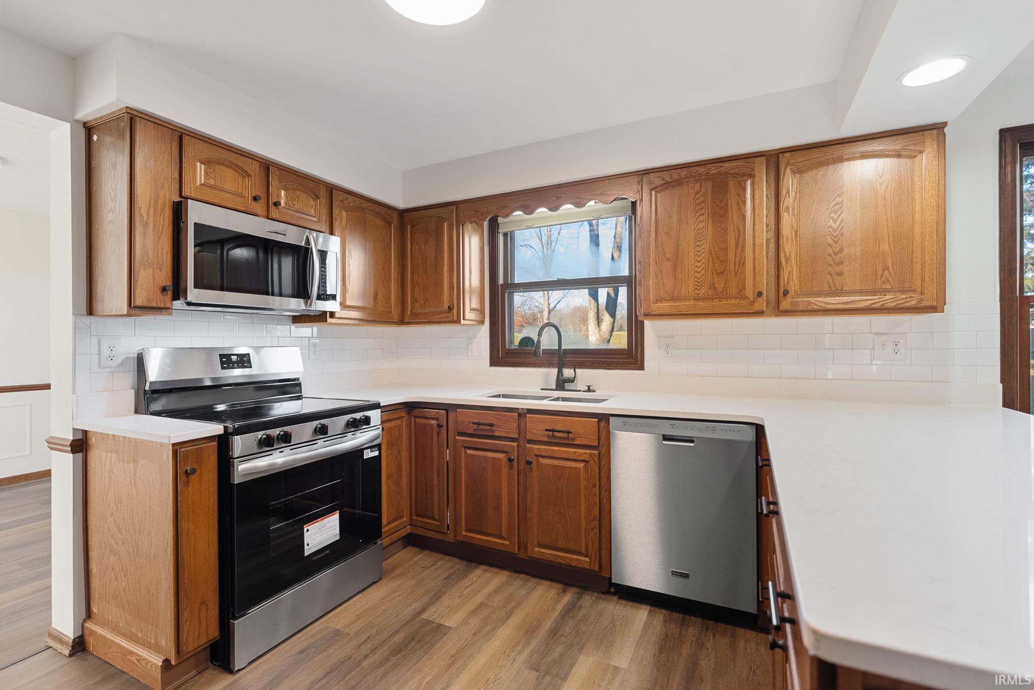 Kitchen with stainless steel appliances, wood finish cabinets, light wood-type flooring, tasteful backsplash, and a peninsula