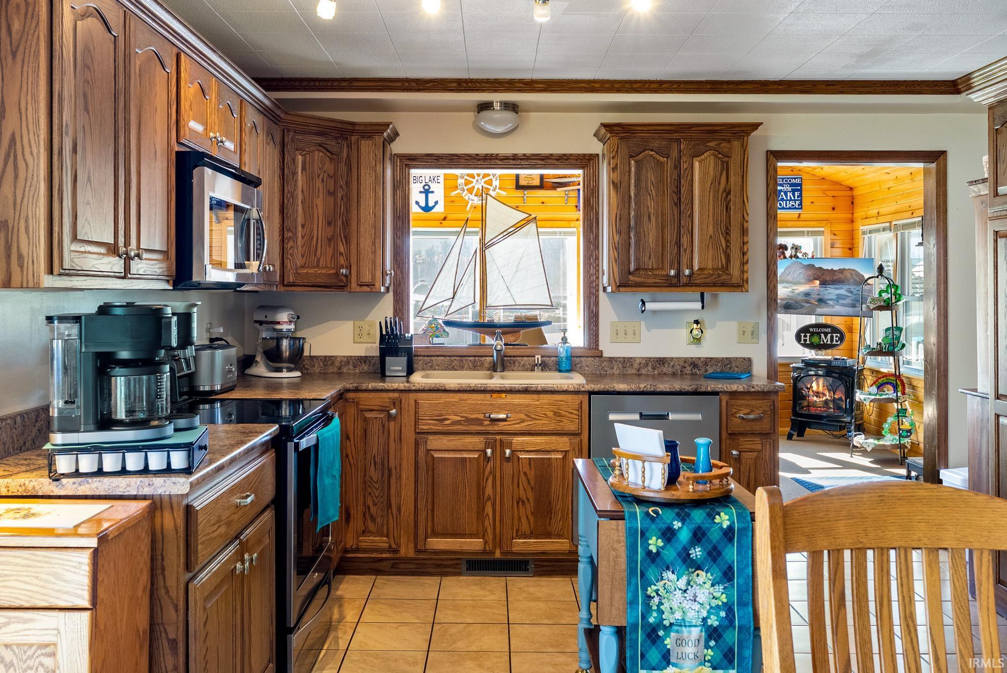Kitchen with crown molding, stainless steel appliances, dark countertops, light tile patterned floors, and wood finish cabinetry