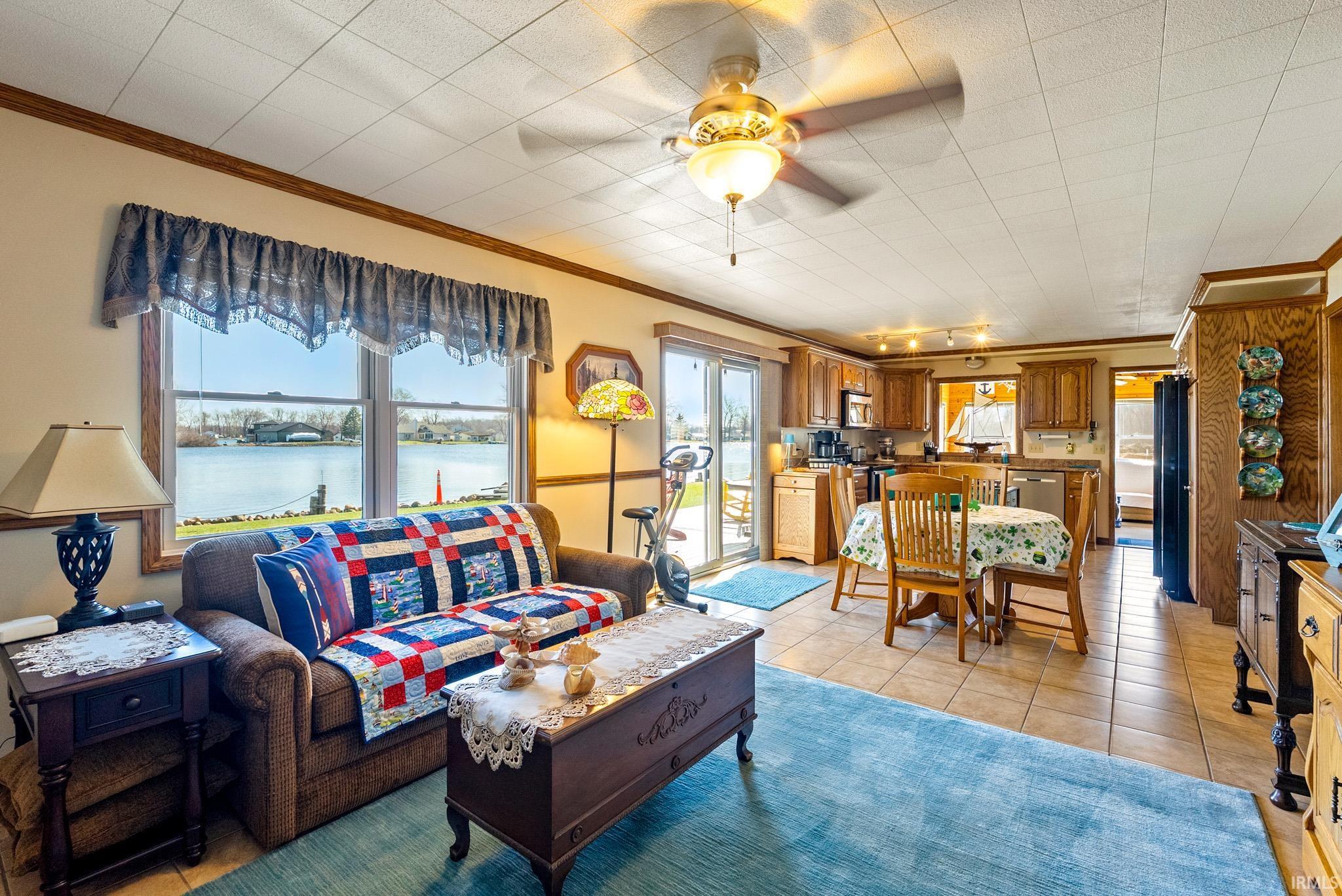 Living area featuring ceiling fan, ornamental molding, light tile patterned flooring, and a water view