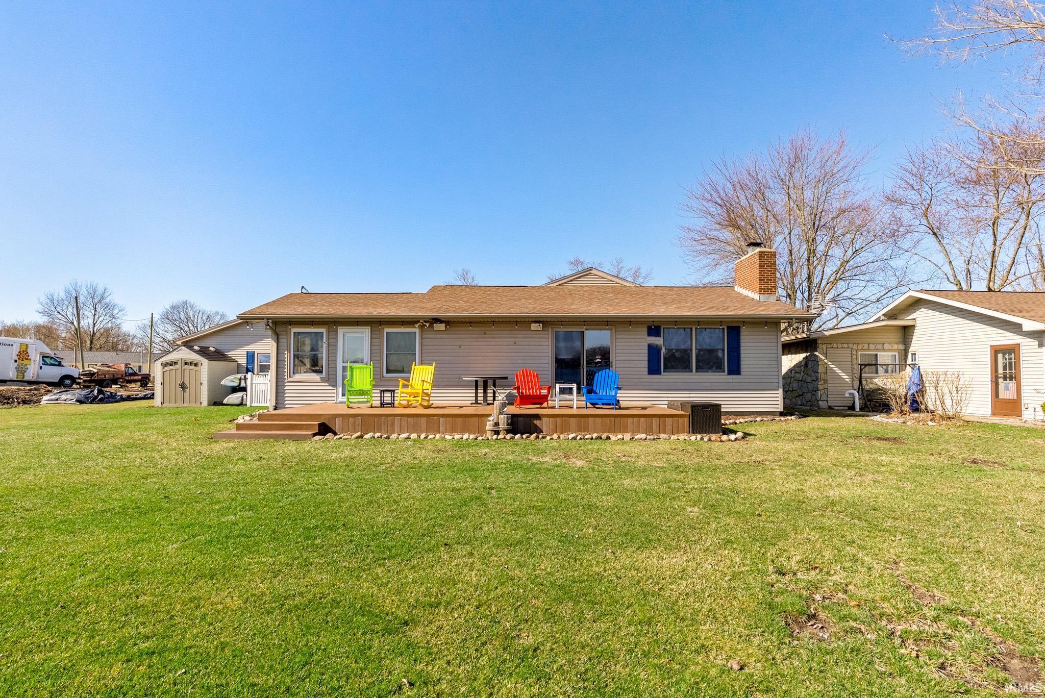 Back of property featuring a storage shed, a wooden deck, a chimney, and a lawn