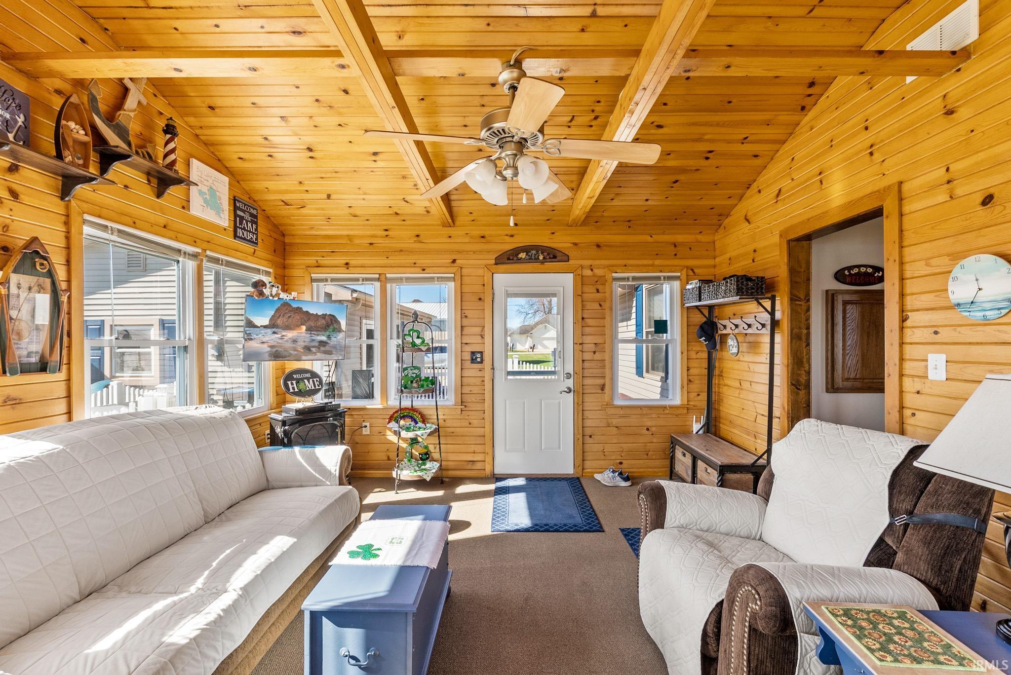 Carpeted living room with wood walls, vaulted ceiling with beams, ceiling fan, and wooden ceiling