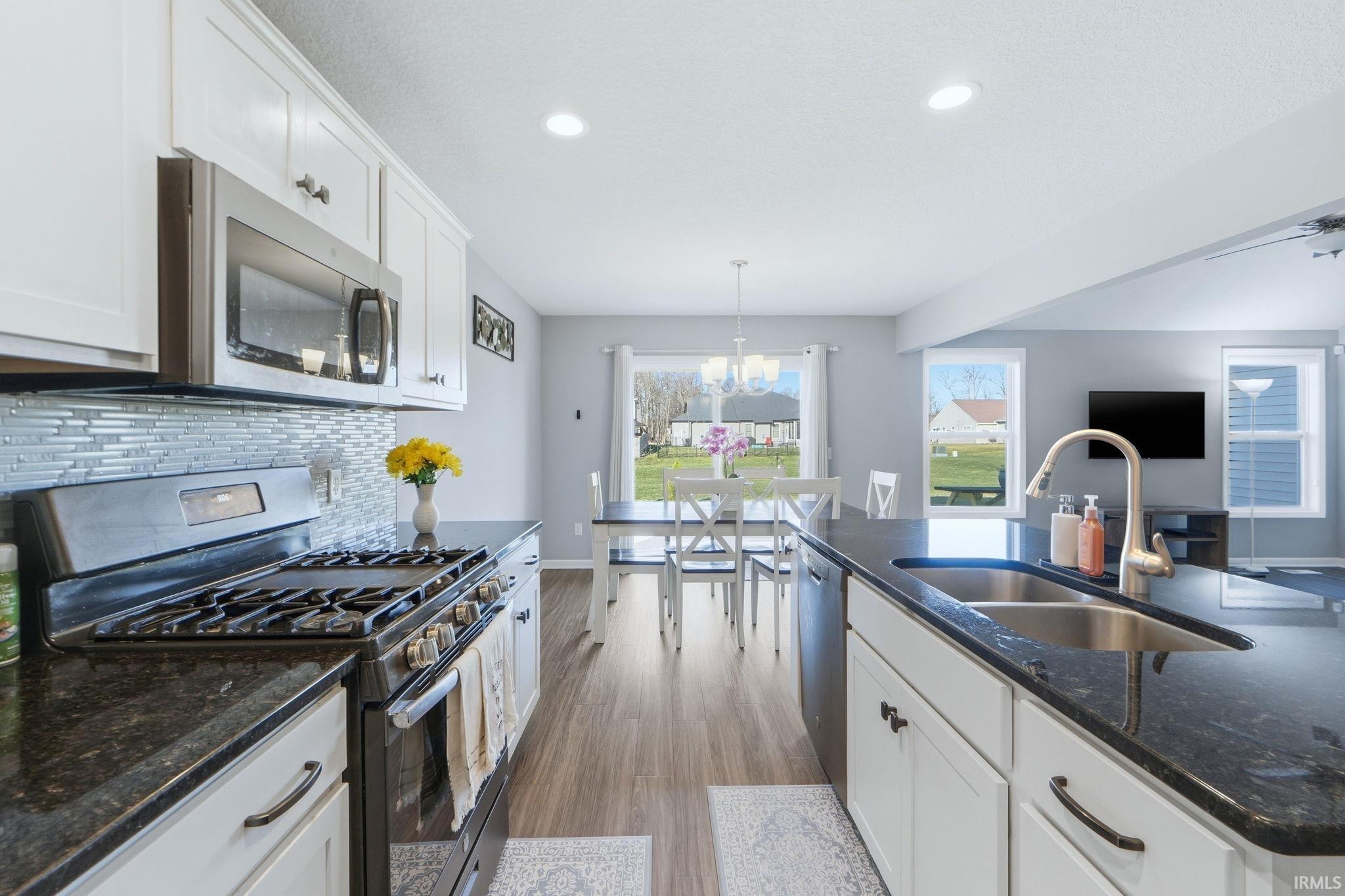 Kitchen with stainless steel appliances, white cabinetry, dark stone countertops, and wood finished floors