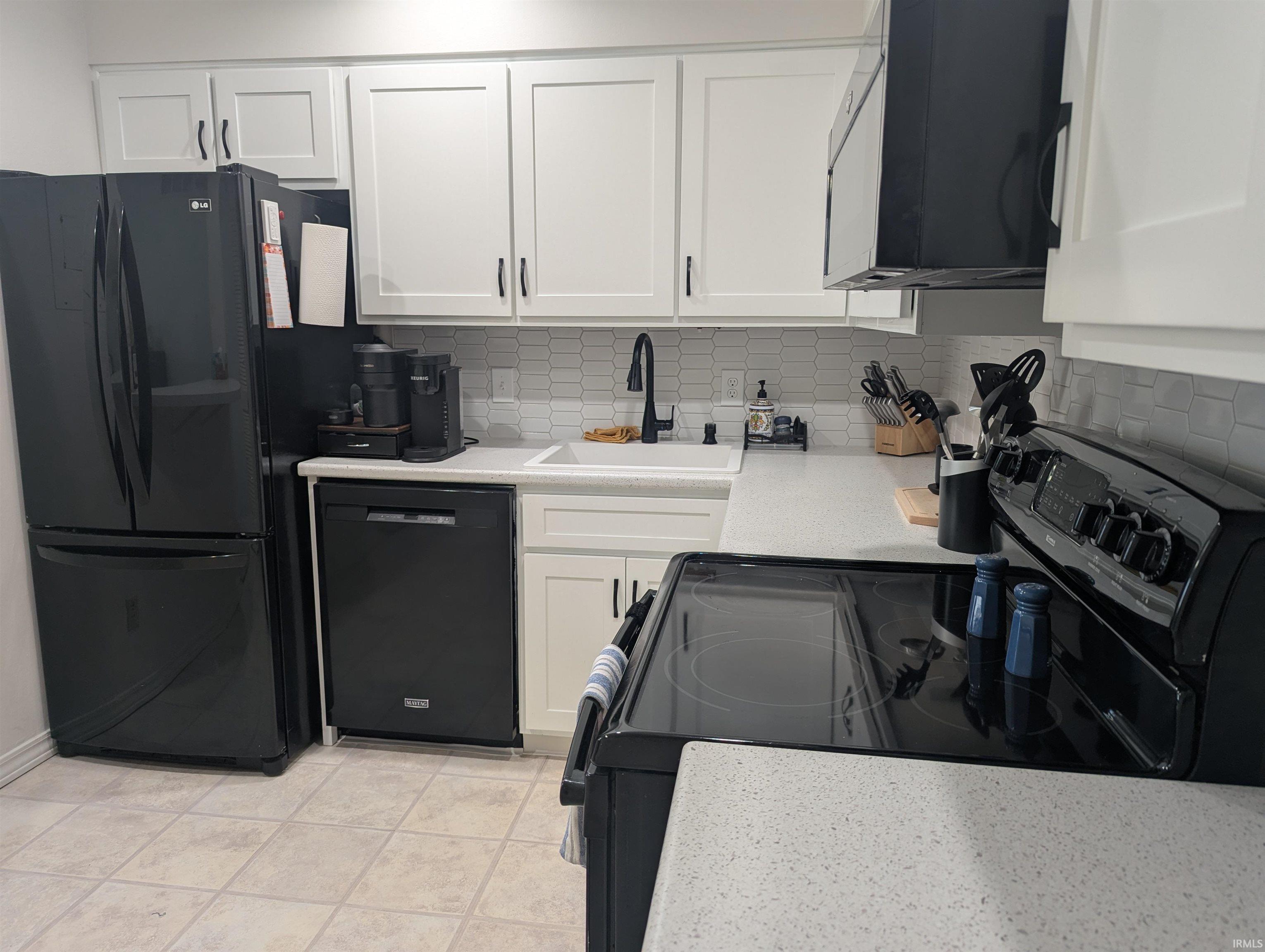 Kitchen featuring black appliances, white cabinetry, and backsplash