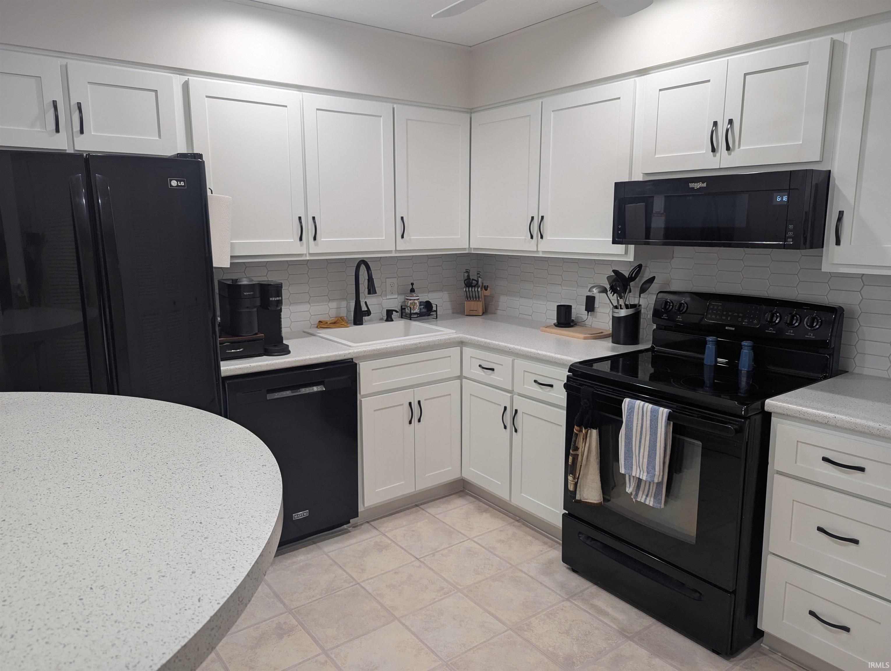 Kitchen with black appliances, white cabinetry, backsplash, and light tile patterned floors