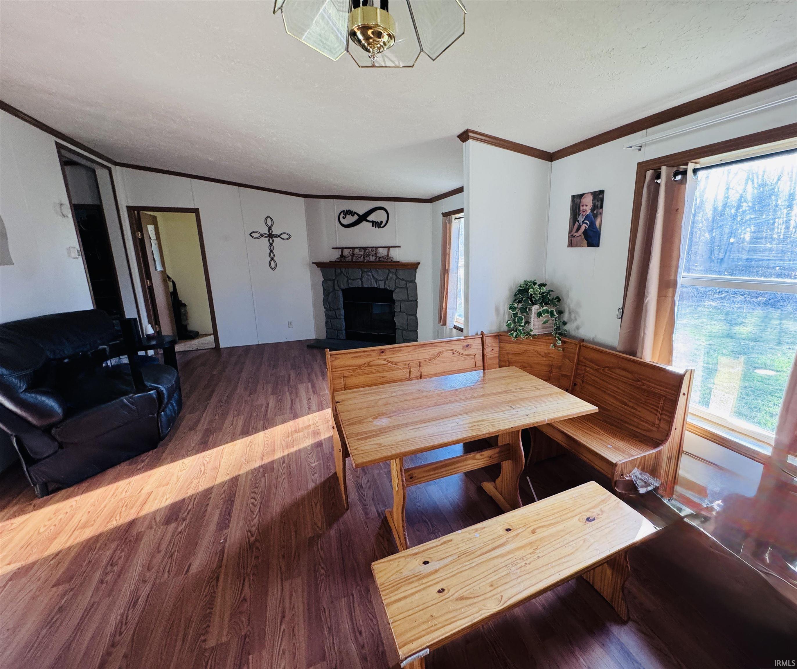 Dining space with ornamental molding, a stone fireplace, plenty of natural light, wood finished floors, and a textured ceiling