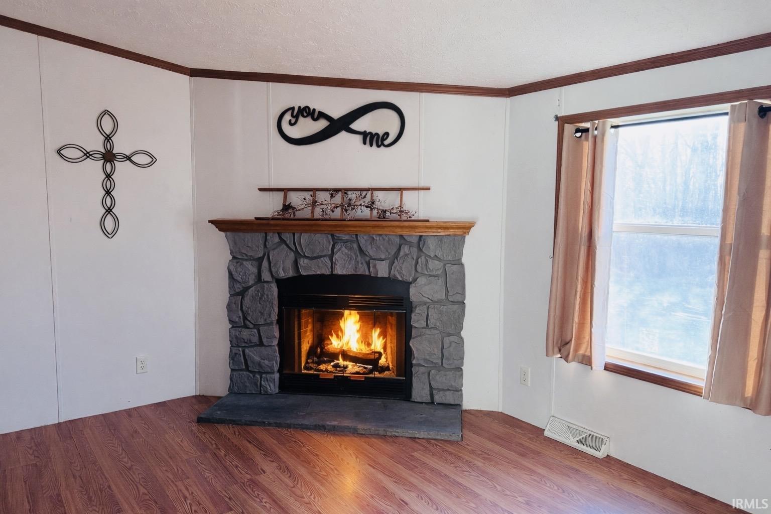 Detailed view of crown molding, a fireplace, wood finished floors, and a textured ceiling