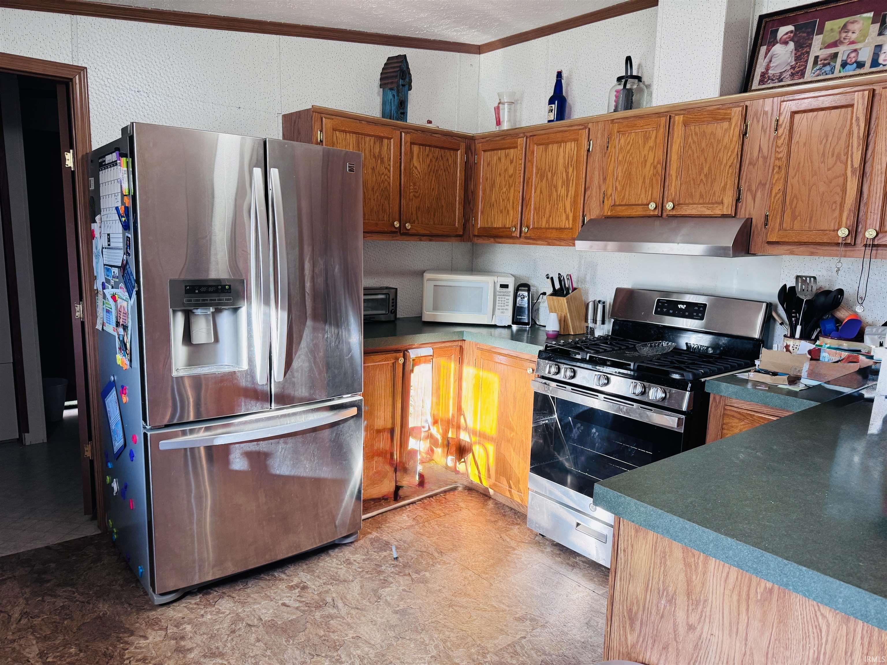 Kitchen featuring stainless steel appliances, wood finish cabinets, dark countertops, and light floors