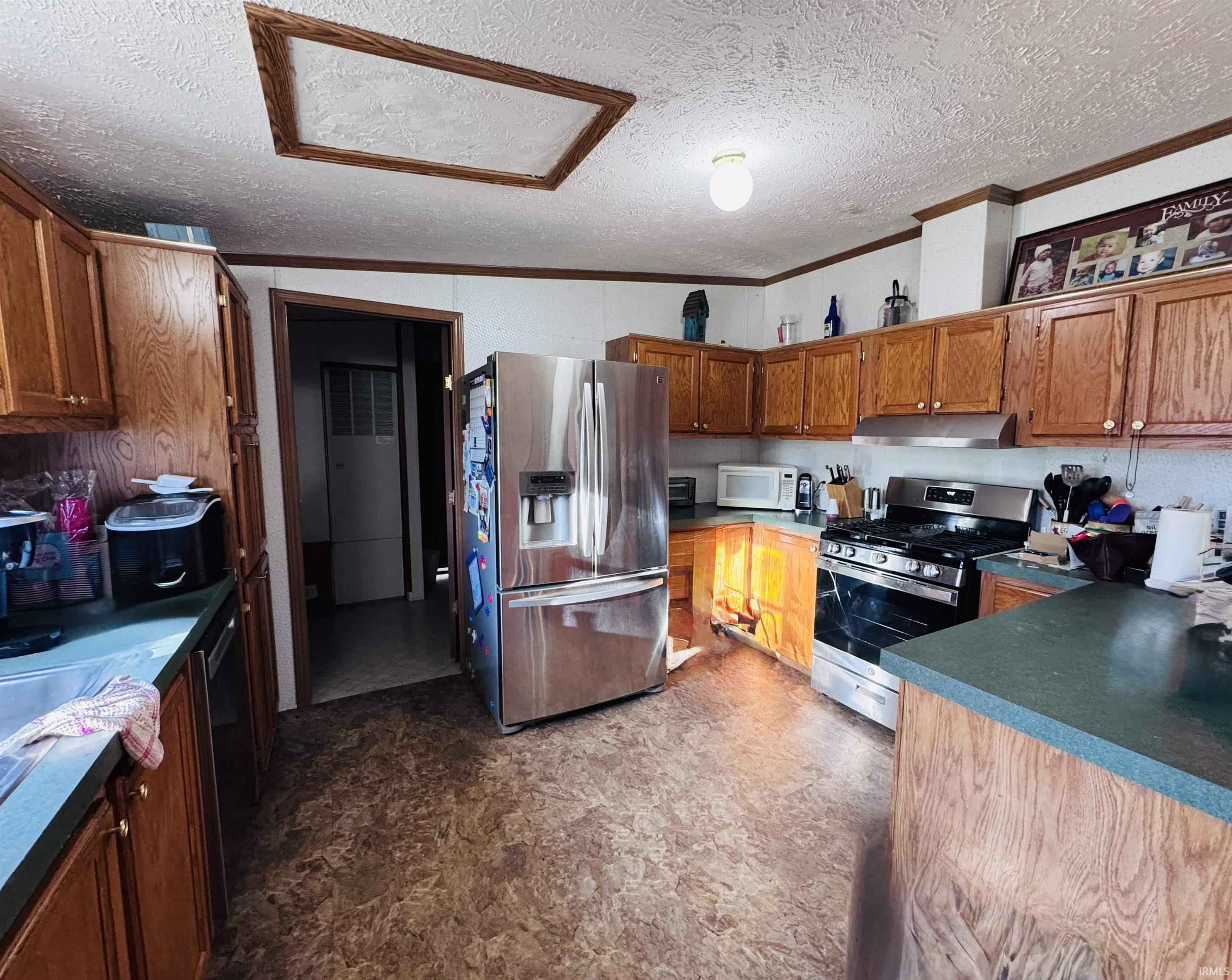 Kitchen featuring dark countertops, stainless steel appliances, wood finish cabinets, crown molding, and a textured ceiling