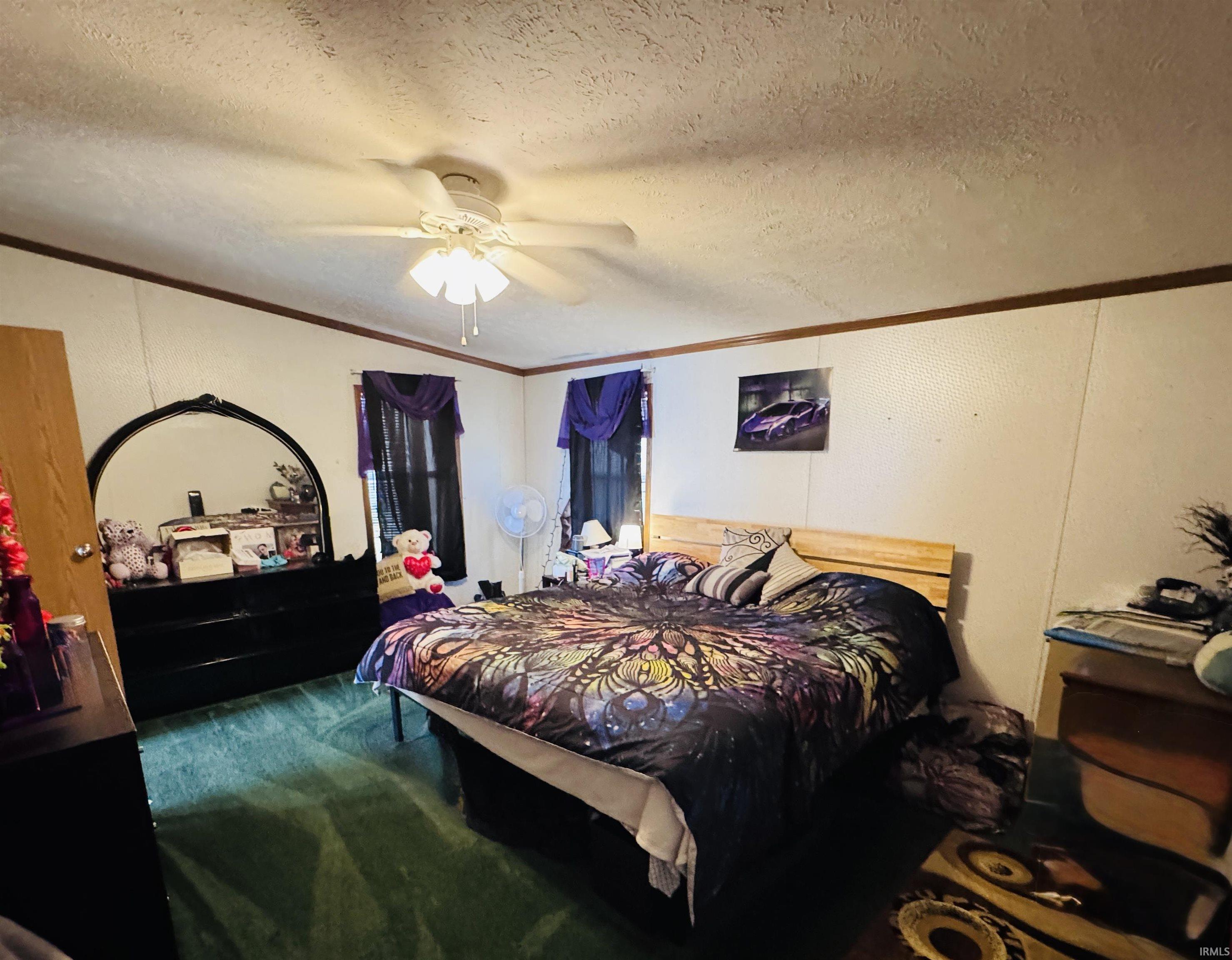 Carpeted bedroom featuring a textured ceiling, ceiling fan, and ornamental molding