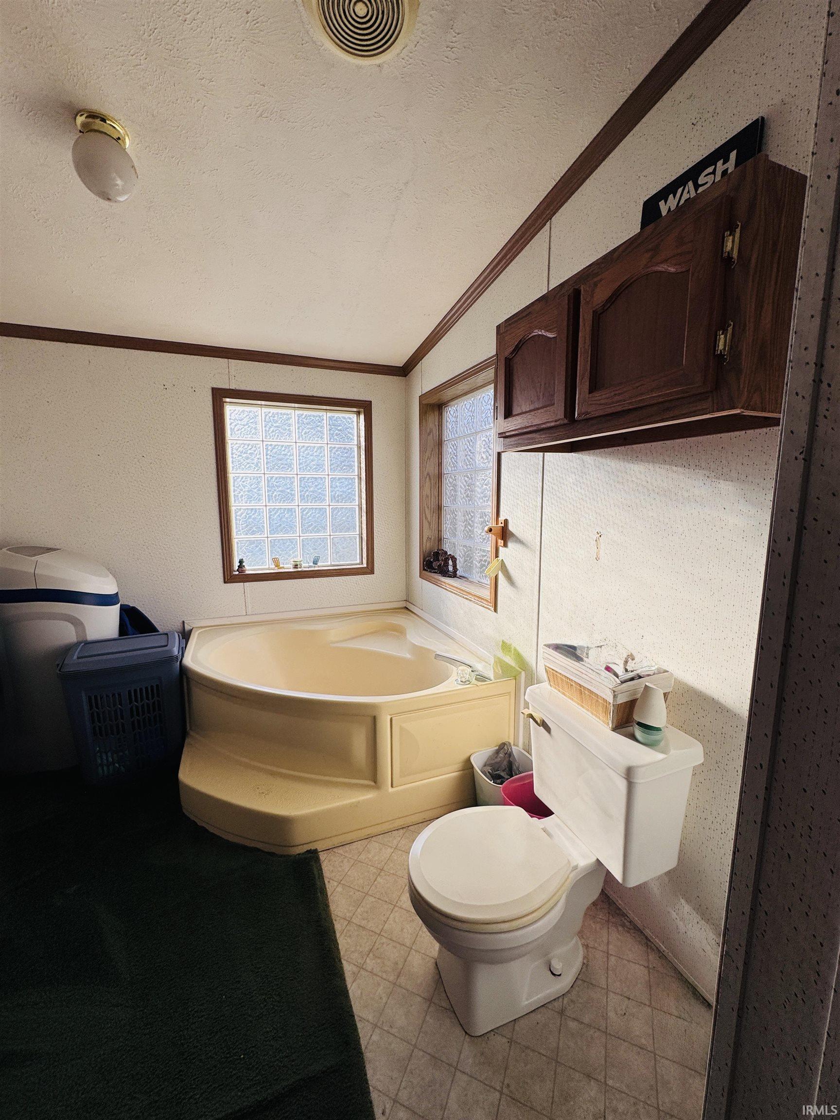 Full bathroom with a garden tub, light floors, a textured ceiling, and ornamental molding