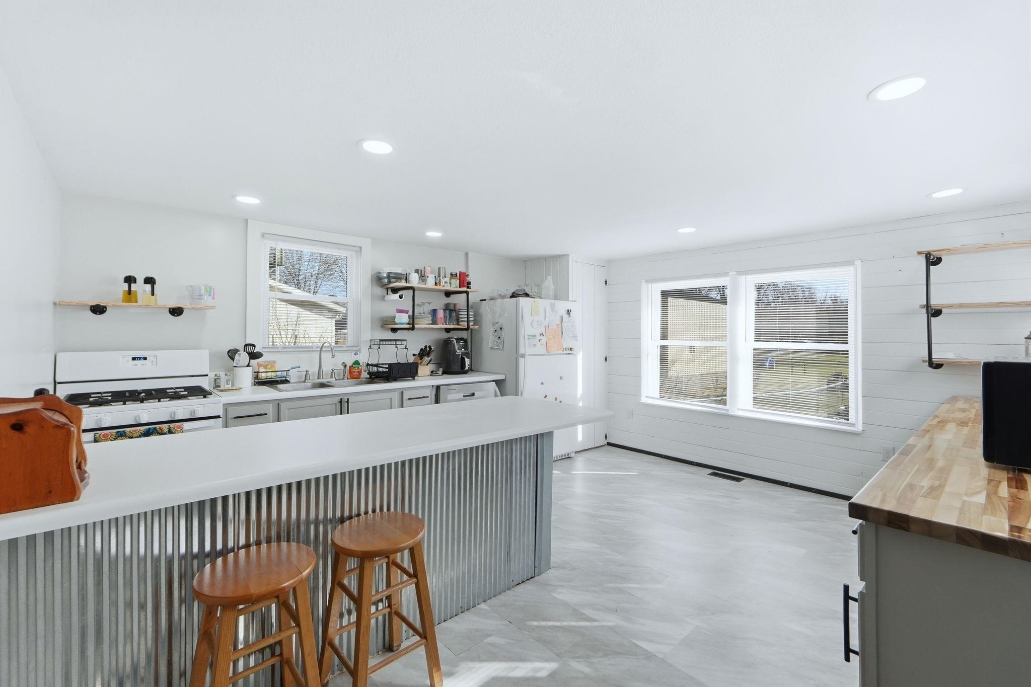 Kitchen featuring butcher block countertops, open shelves, a breakfast bar area, white appliances, and wood walls