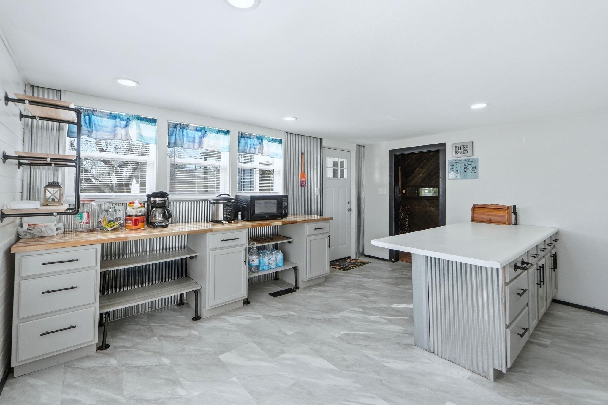 Kitchen featuring a peninsula, gray cabinets, black microwave, light flooring, and butcher block counters