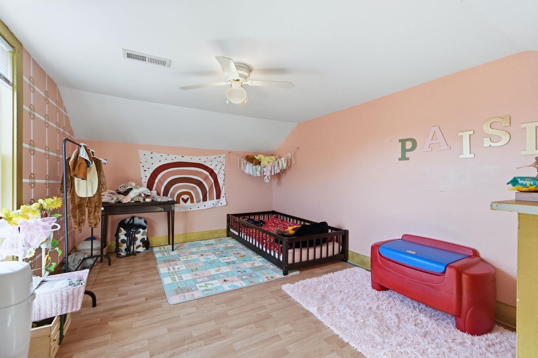 Bedroom with lofted ceiling, a crib, light wood-style flooring, and a ceiling fan