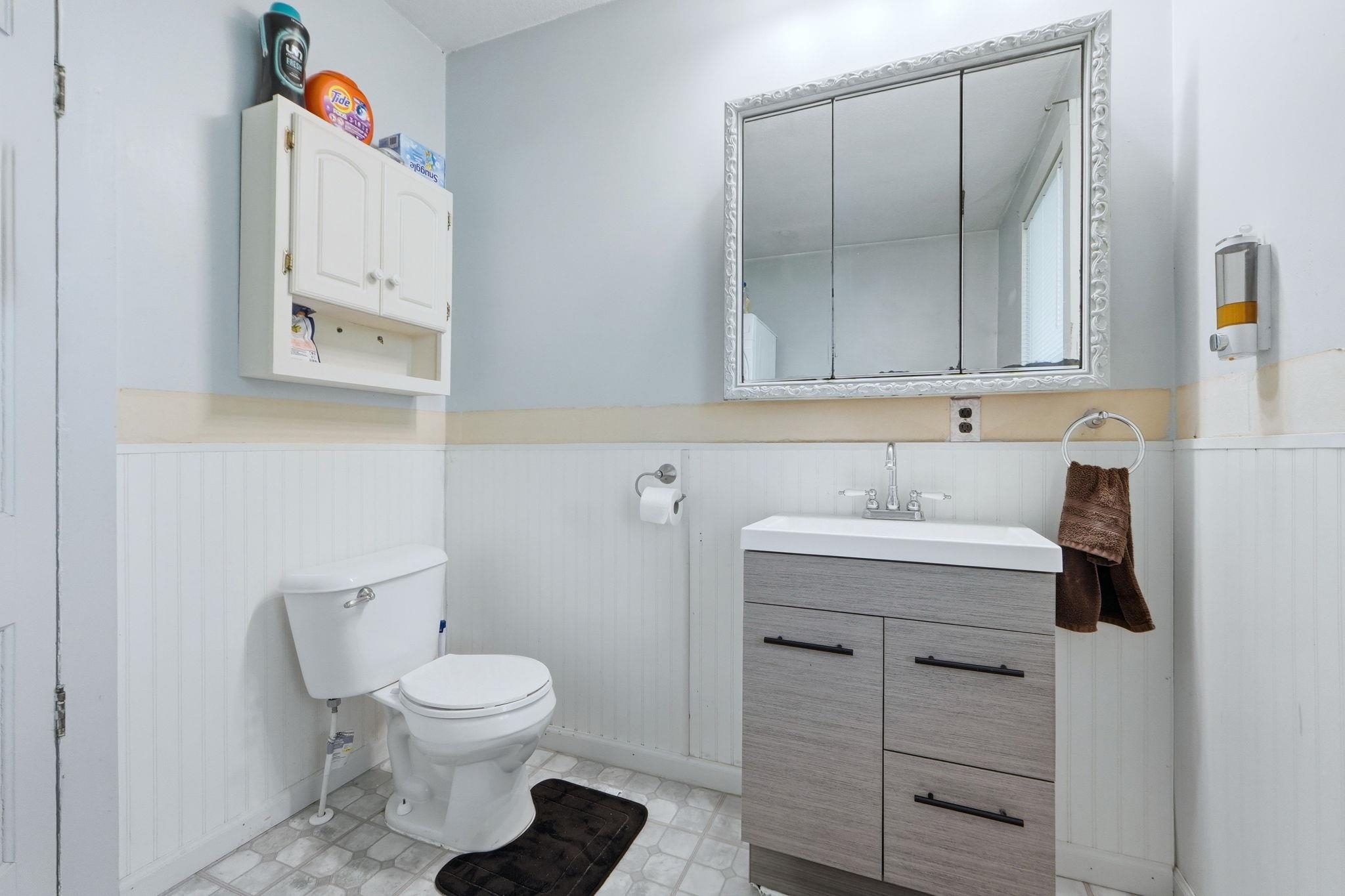 Half bath with vanity, a wainscoted wall, and light flooring