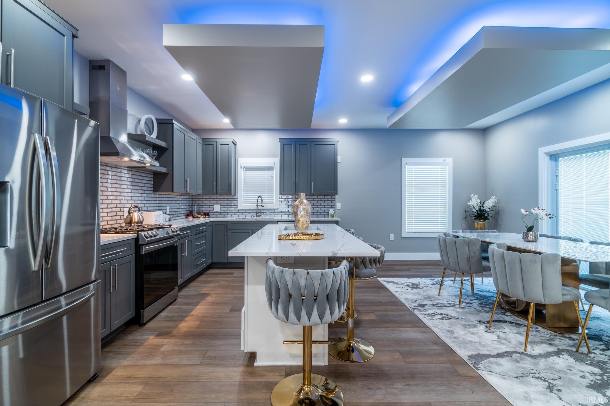 Kitchen featuring stainless steel appliances, a kitchen bar, a center island, light stone countertops, and dark wood-type flooring