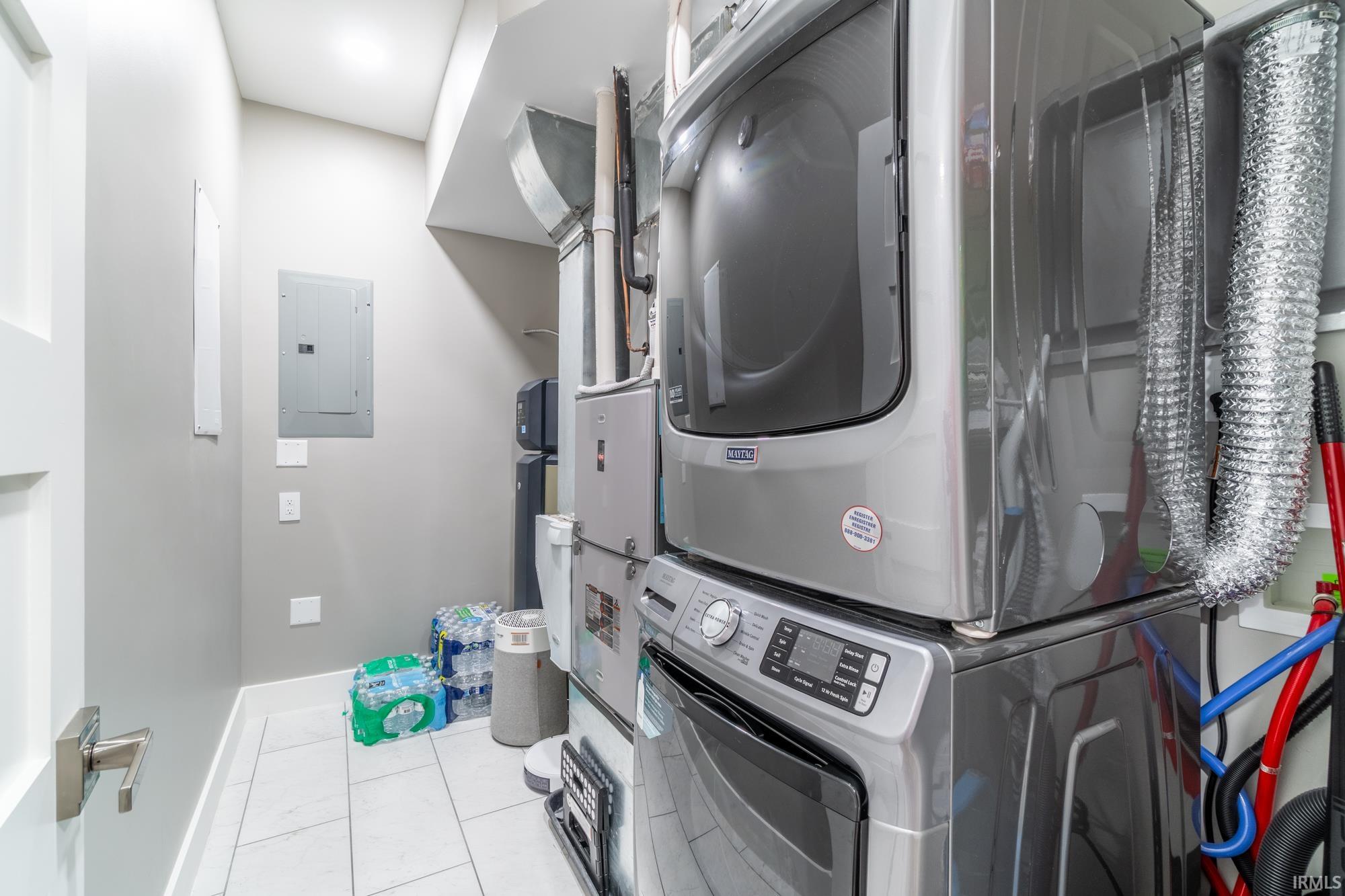 Laundry room featuring stacked washing machine and dryer, electric panel, and light tile patterned floors