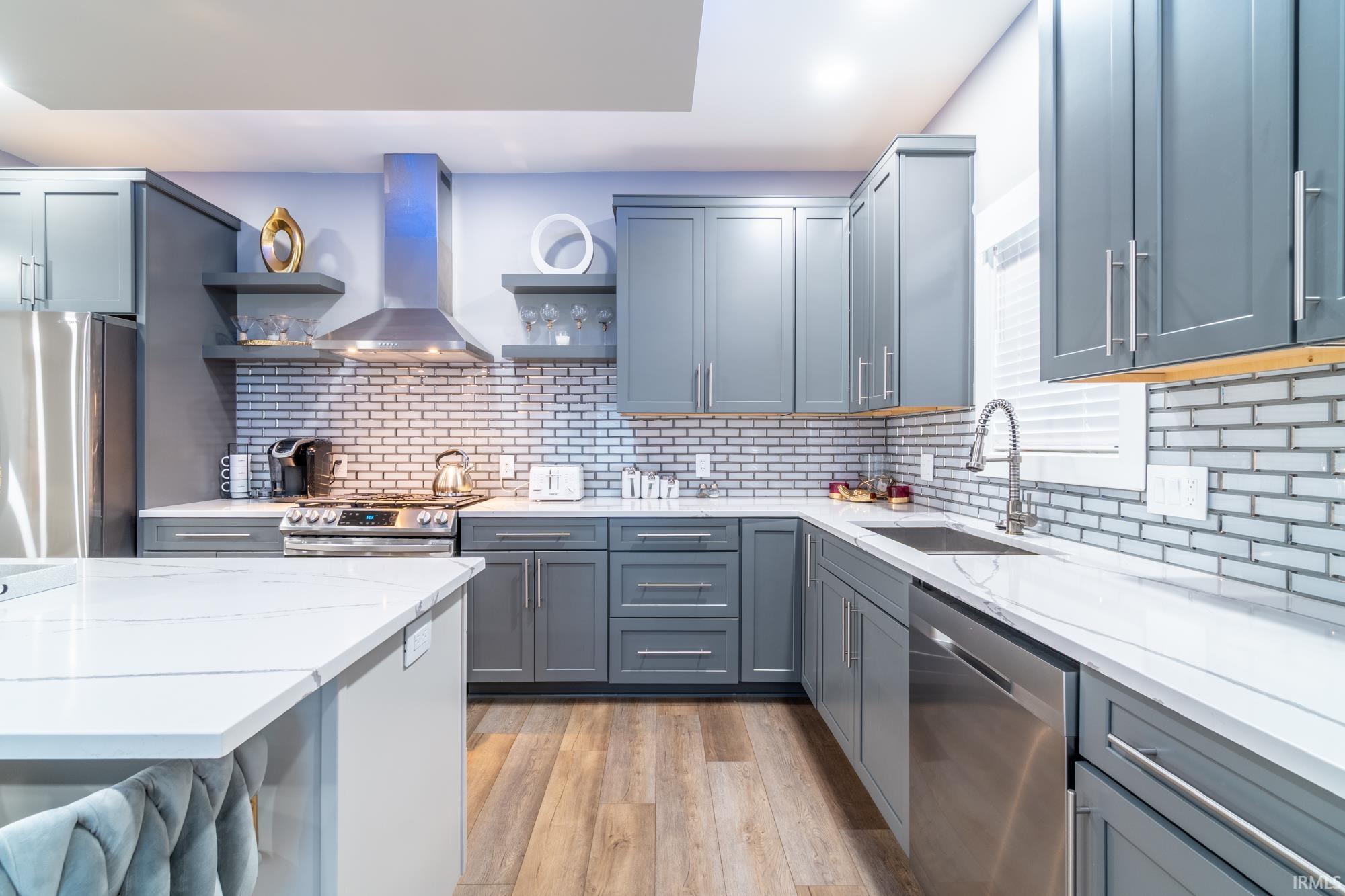 Kitchen with open shelves, stainless steel appliances, light stone counters, light wood-type flooring, and tasteful backsplash