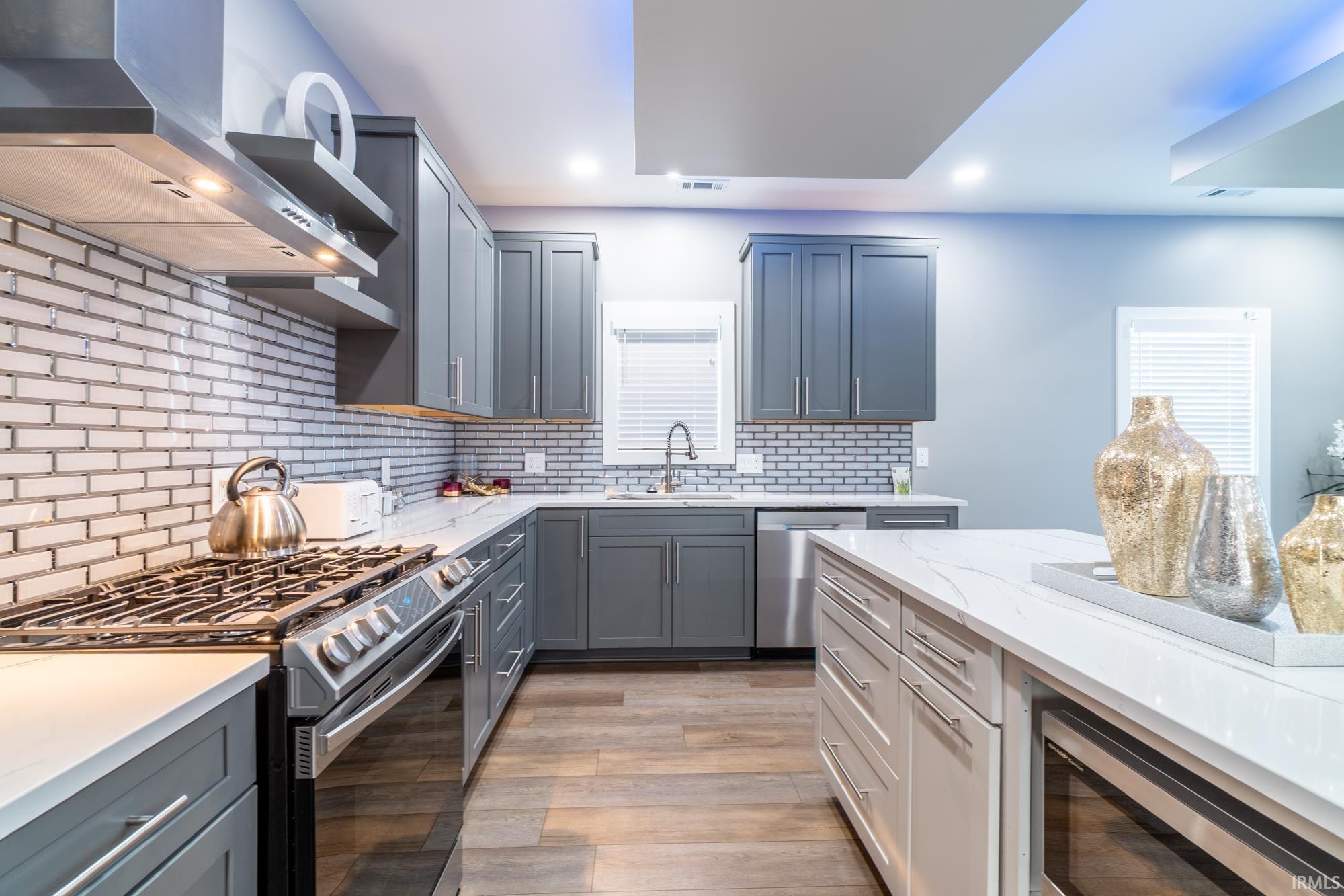 Kitchen featuring stainless steel appliances, light stone countertops, light wood finished floors, gray cabinetry, and tasteful backsplash