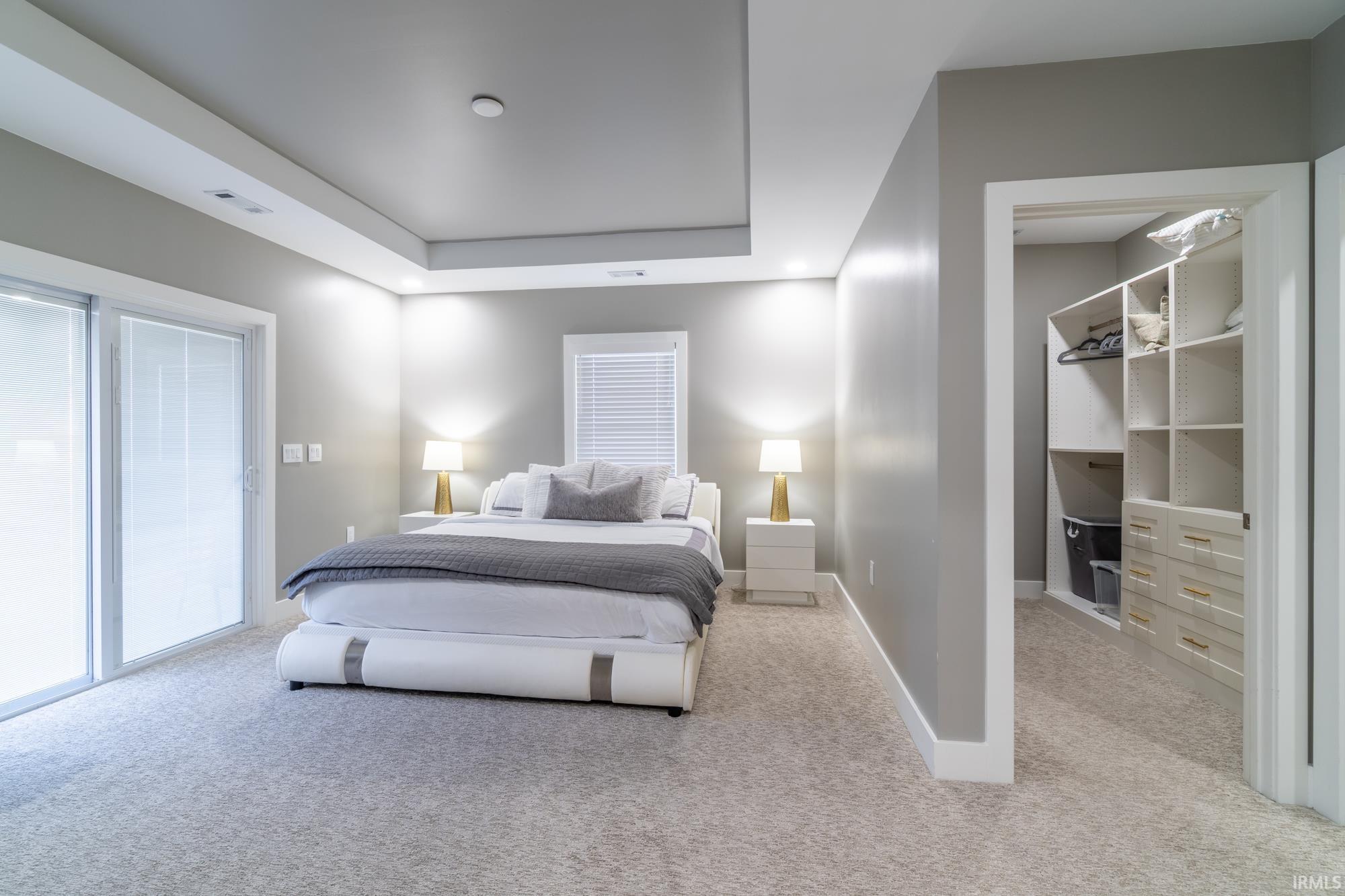 Bedroom with light carpet, a walk in closet, and a raised ceiling