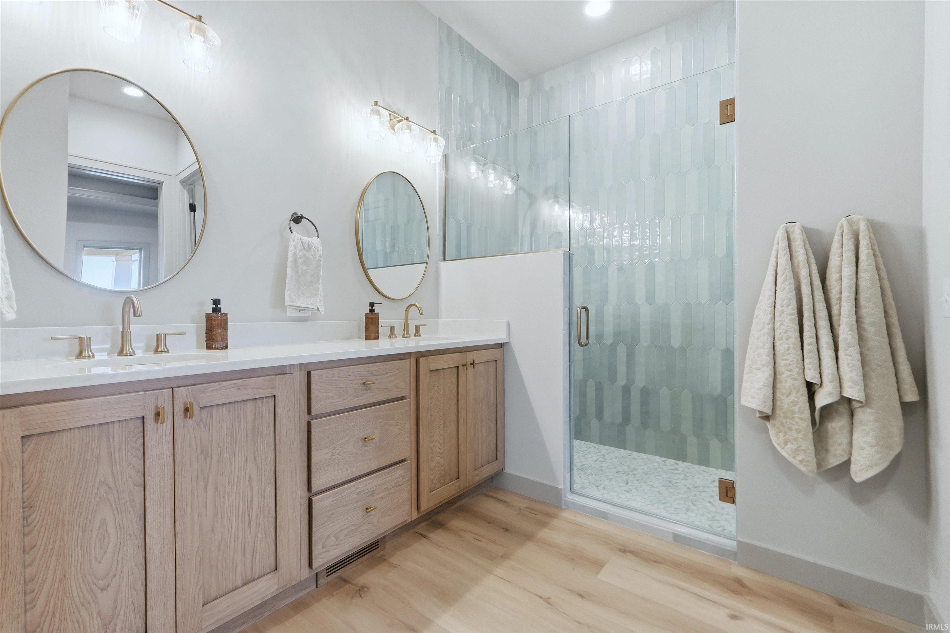 Bathroom featuring double vanity, a stall shower, light wood finished floors, and recessed lighting