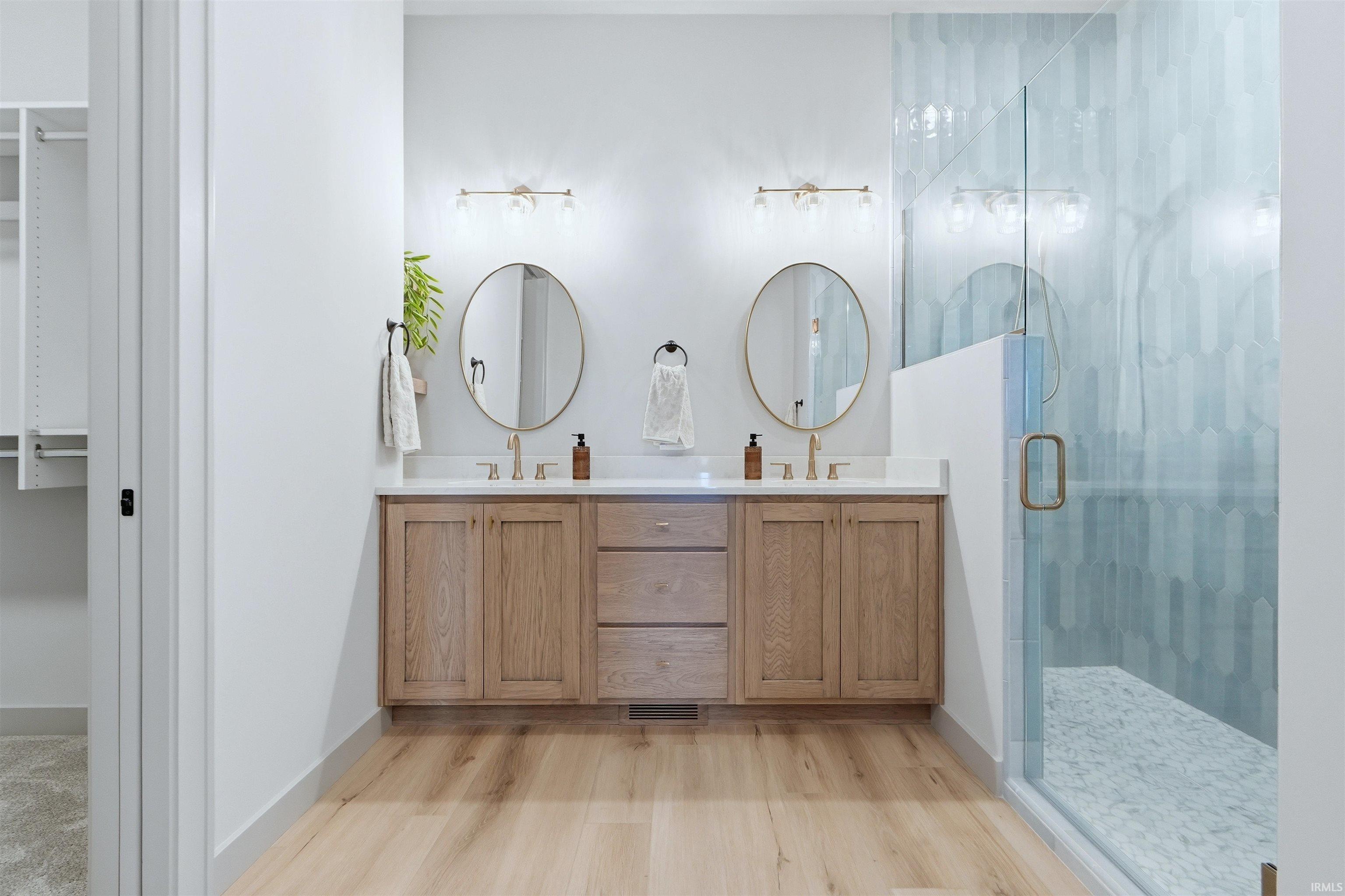 Bathroom featuring double vanity, a marble finish shower, and light wood-style flooring