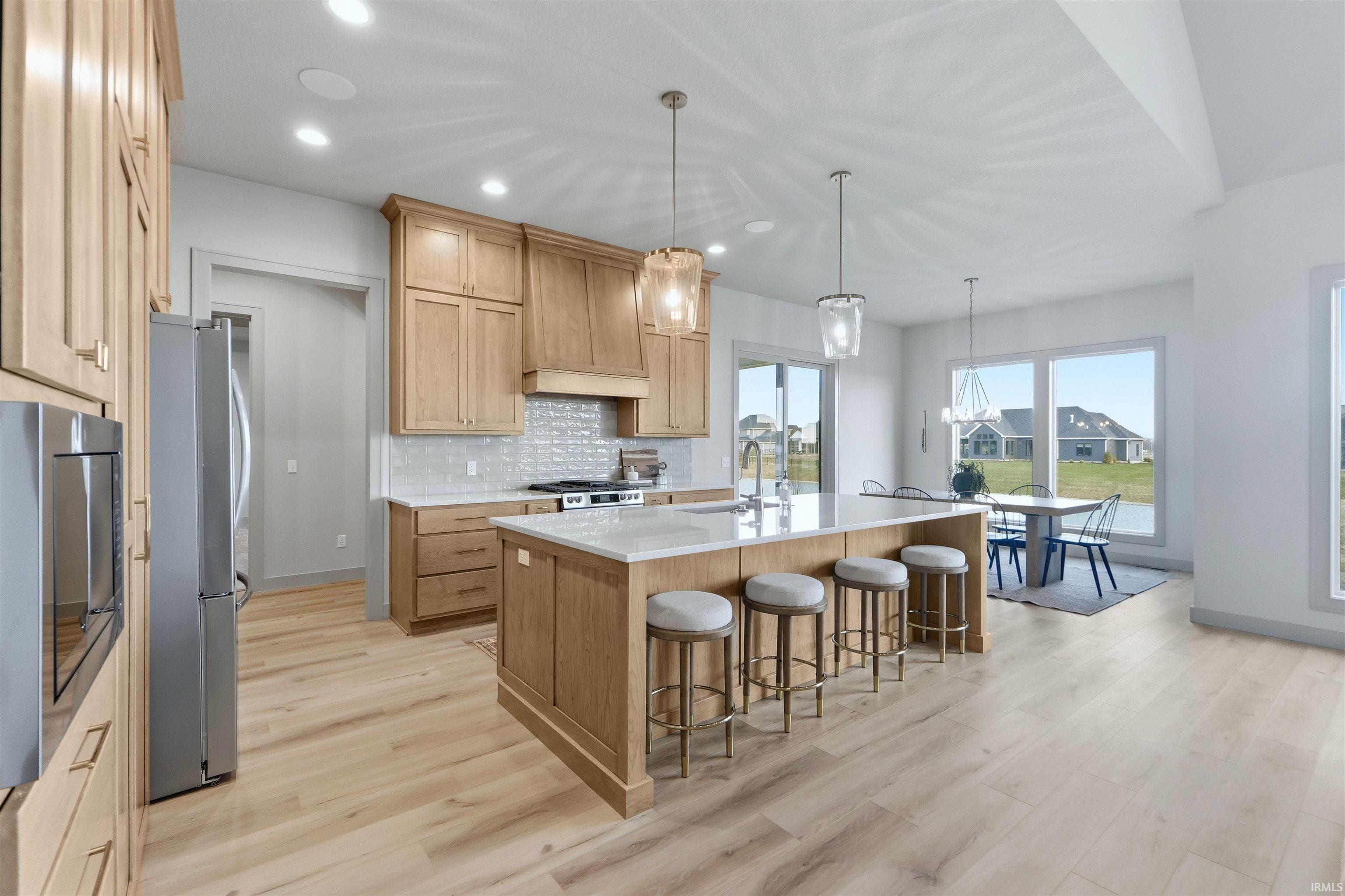 Kitchen with an island with sink, a breakfast bar area, light wood-style flooring, stainless steel appliances, and decorative backsplash
