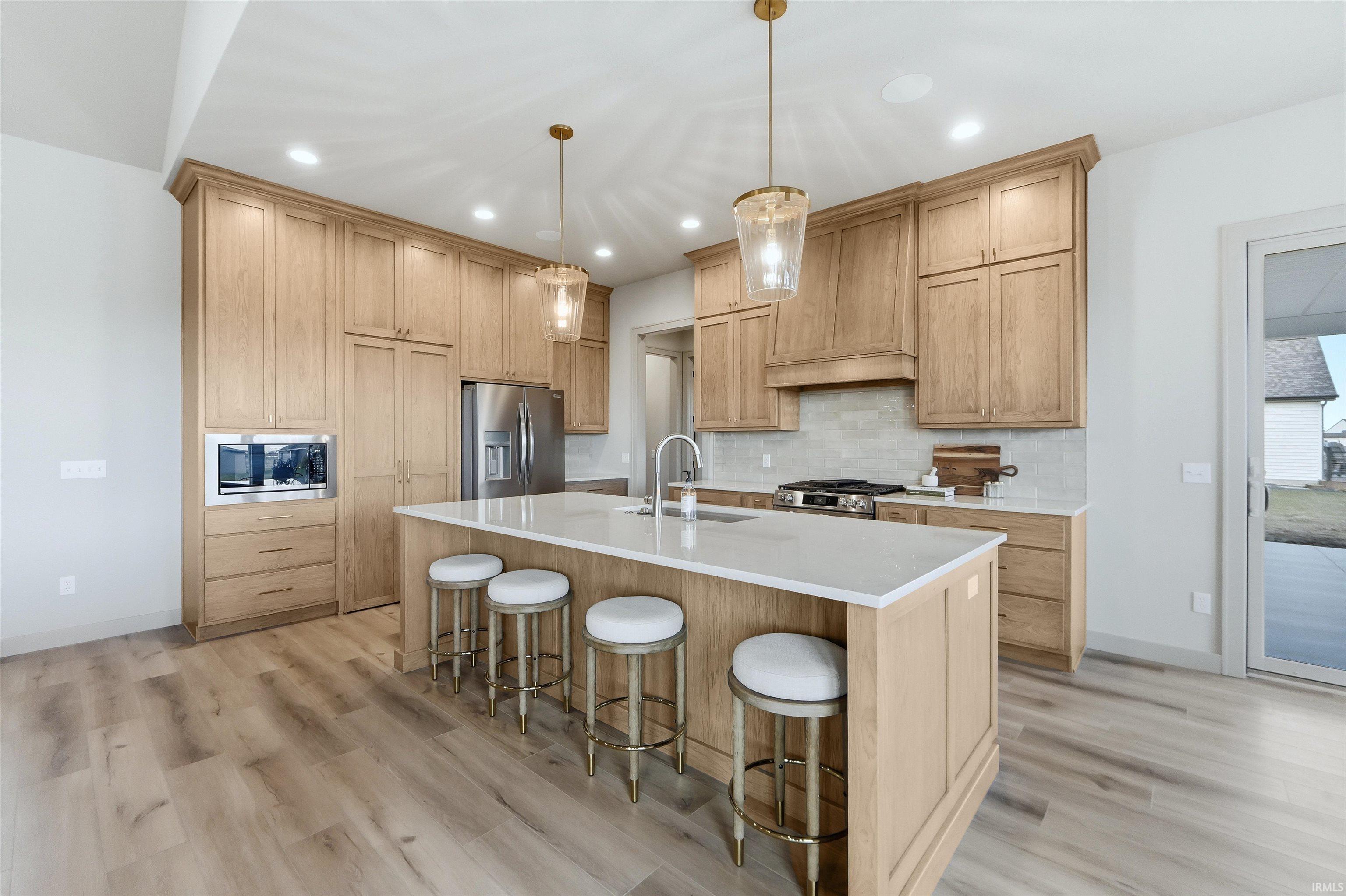 Kitchen featuring a breakfast bar, a center island with sink, stainless steel appliances, and light wood-style floors