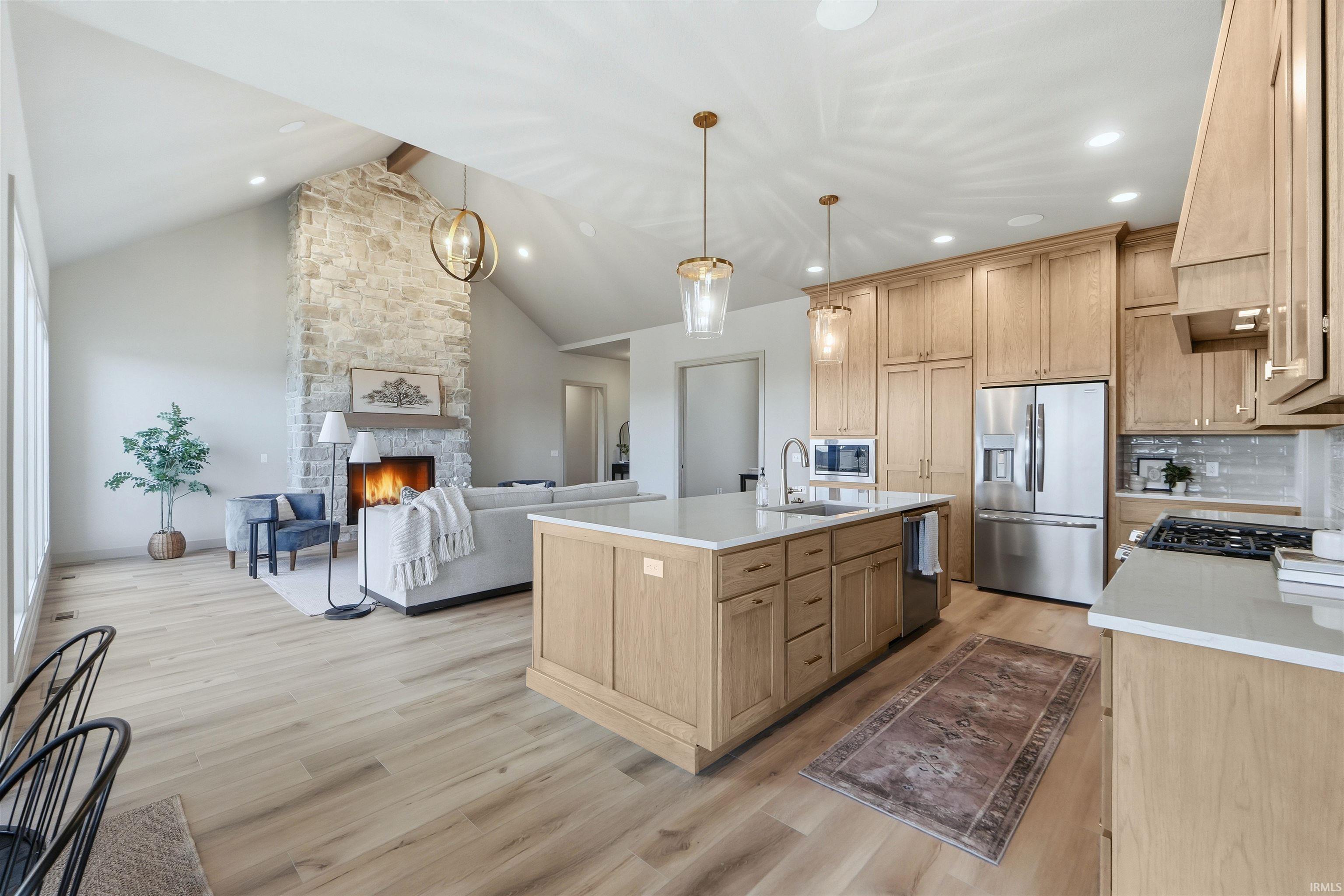 Kitchen with a kitchen island with sink, open floor plan, light wood-type flooring, a stone fireplace, and light wood finish cabinets