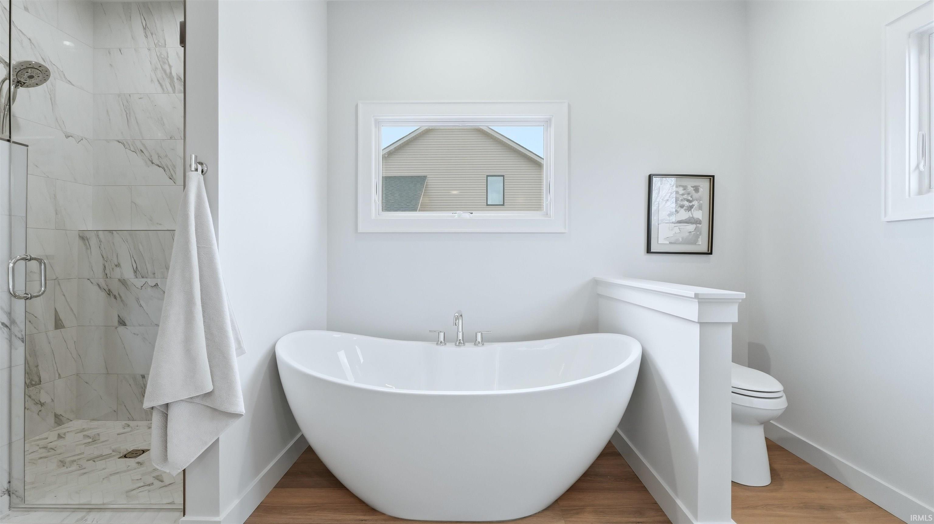 Bathroom featuring a marble finish shower, light wood-type flooring, and a freestanding tub
