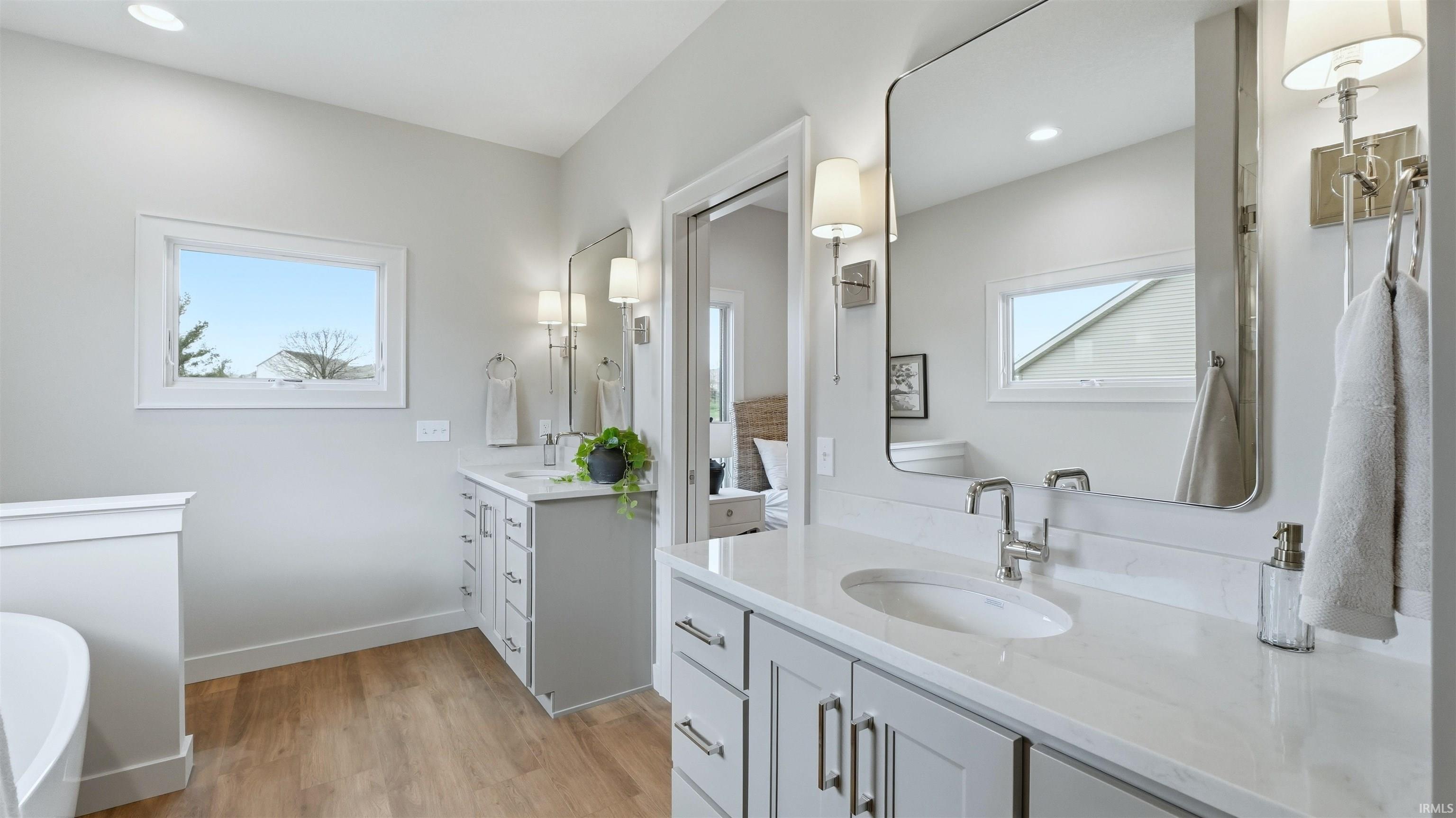 Full bath with two vanities, light wood-type flooring, and a freestanding bath