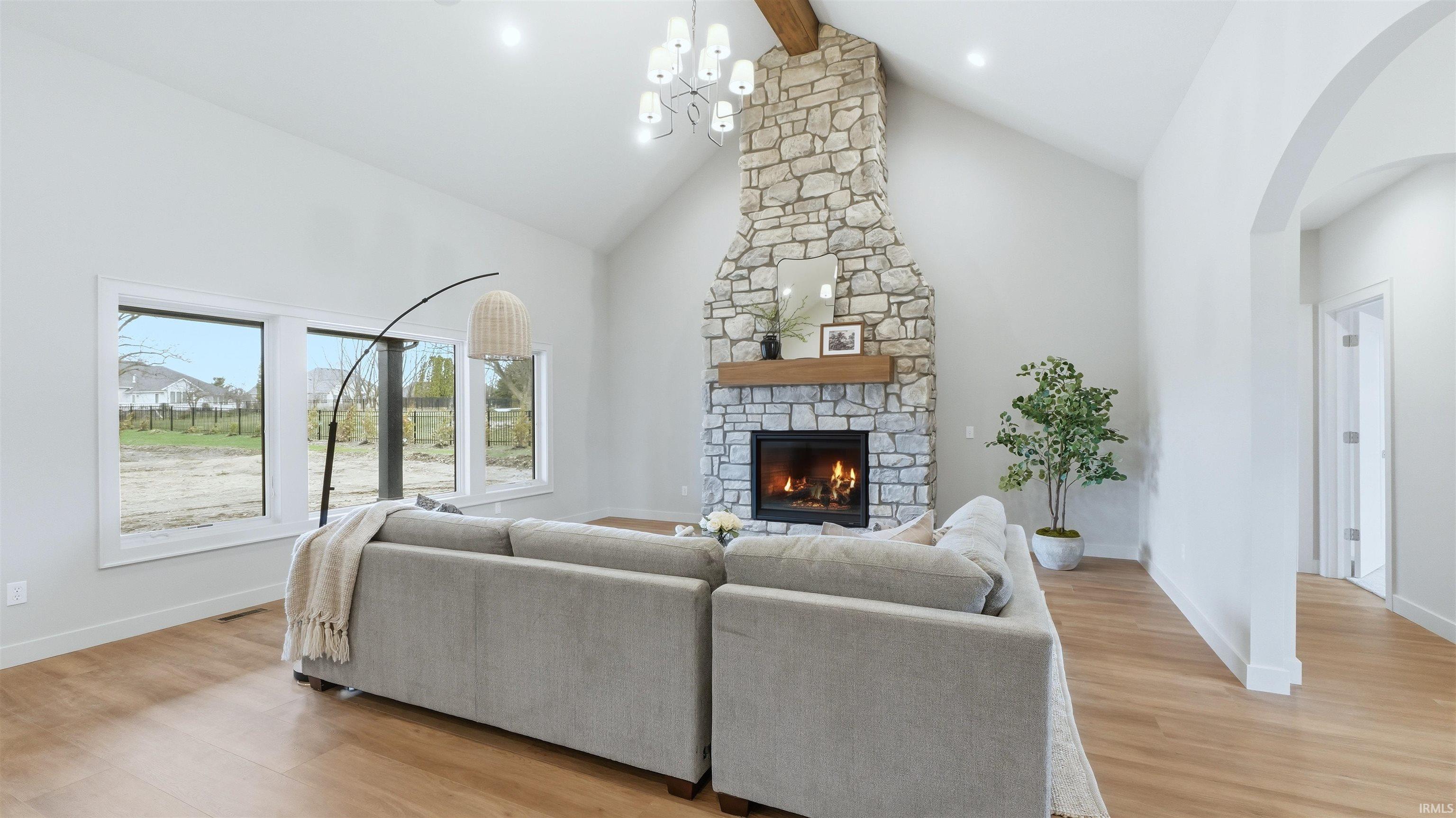 Living room featuring light wood-style flooring, a fireplace, lofted ceiling, and arched walkways