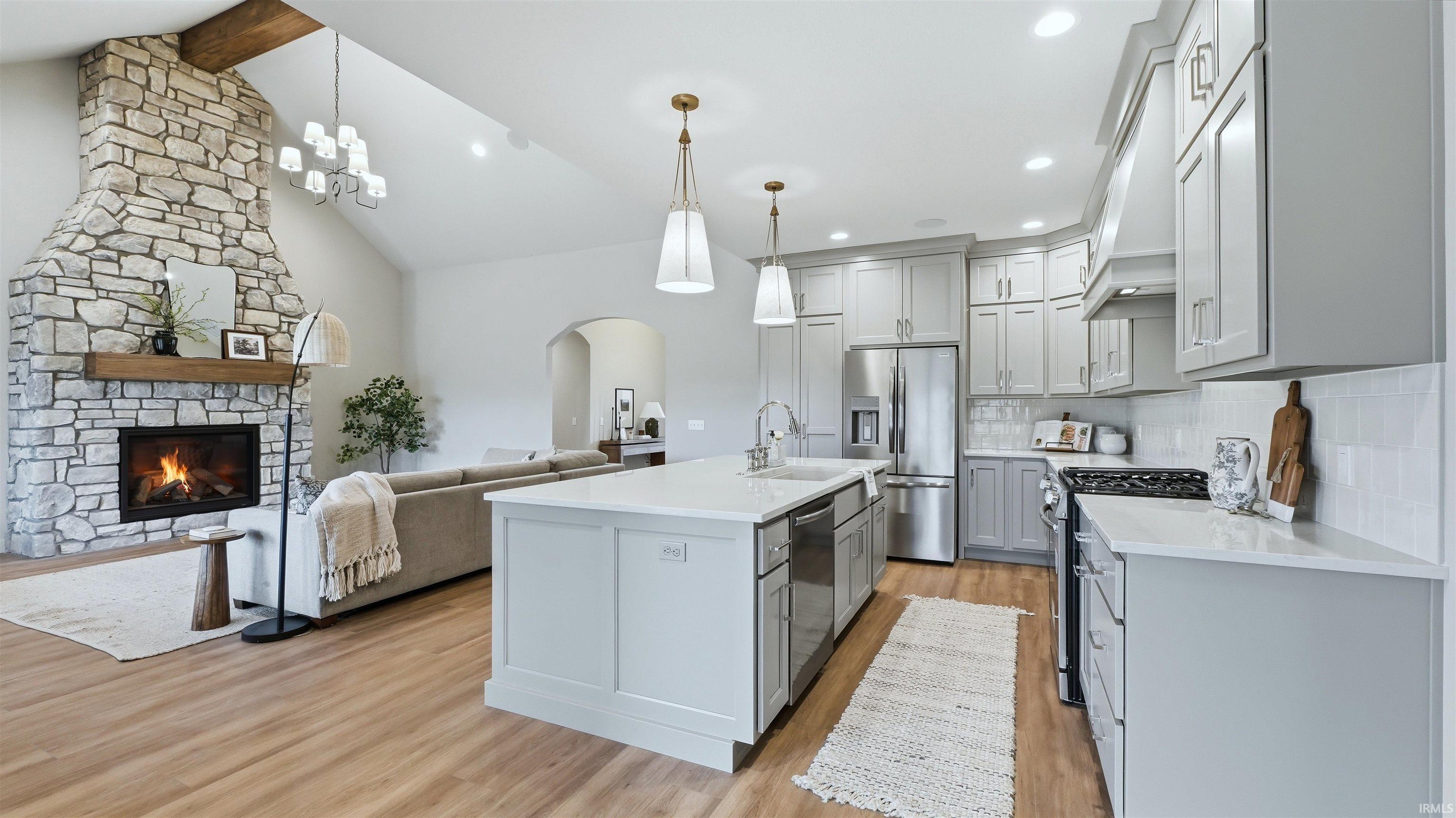 Kitchen with arched walkways, light wood finished floors, stainless steel appliances, a fireplace, and open floor plan